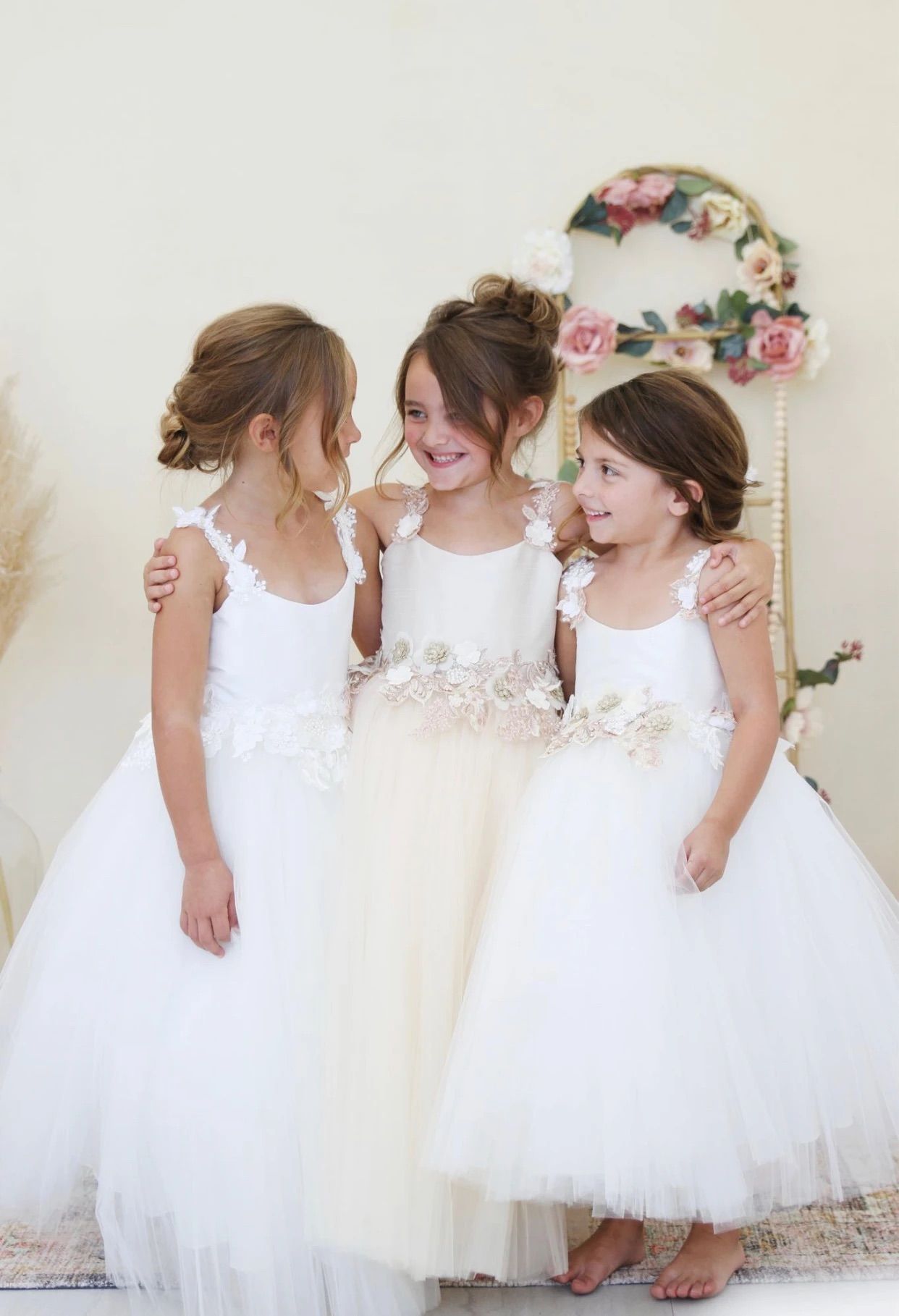 Three flower girls are standing next to each other in white dresses.