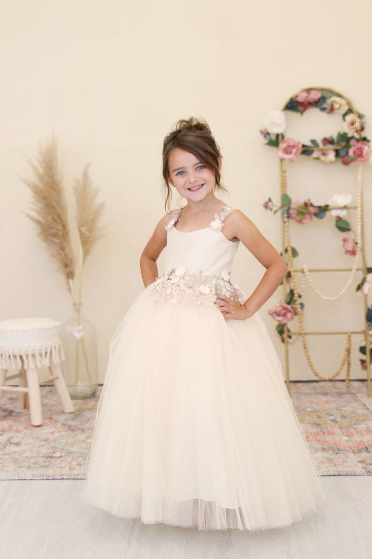 A little girl in a white flower girl dress is standing in a room.