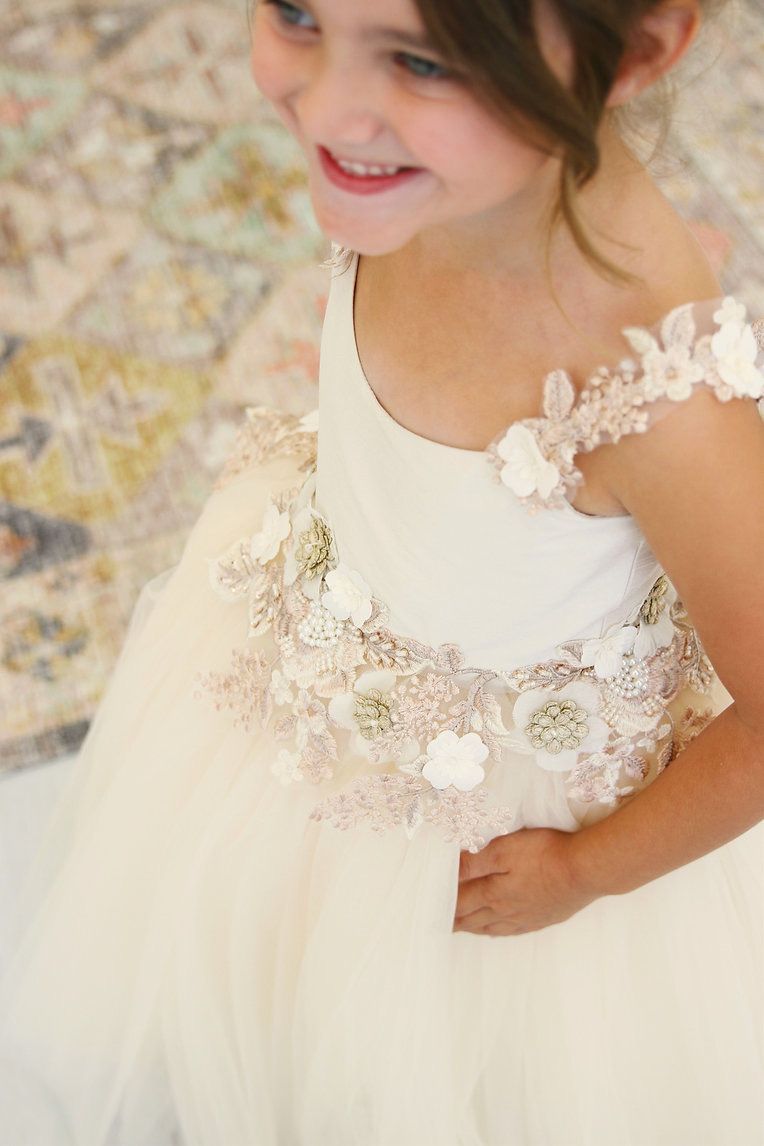 A little girl is wearing a white flower girl dress and smiling.