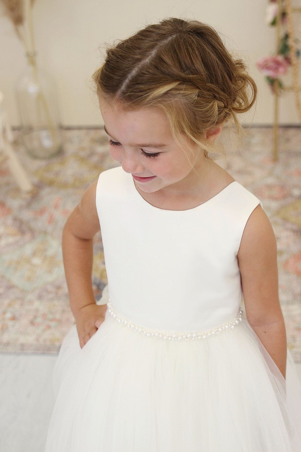 A little girl is wearing a white dress with pearls on the waist.