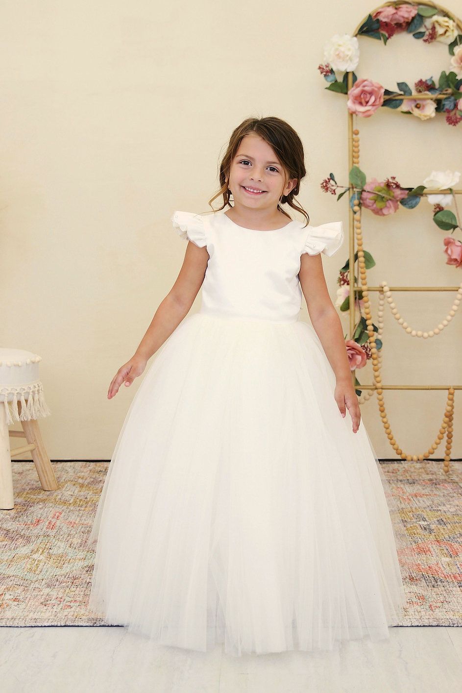A little girl in a white dress is standing in a room.