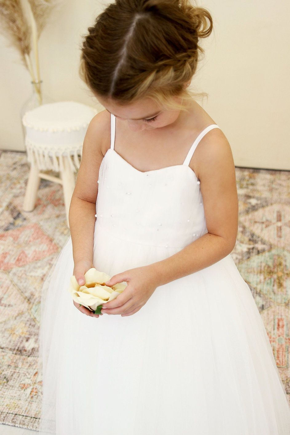 A little girl in a white dress is holding a flower in her hand.