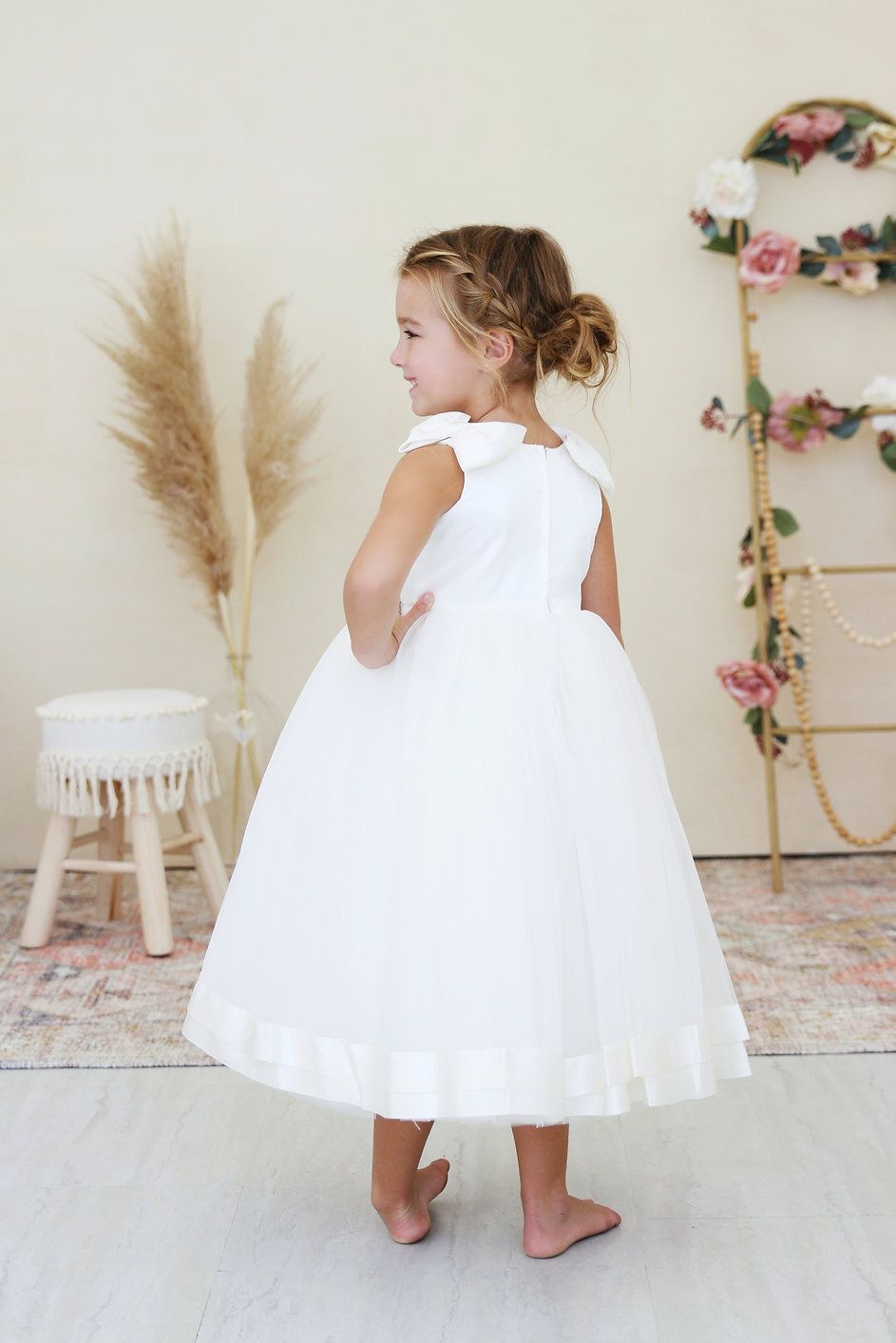 A little girl in a white dress is standing in a room.