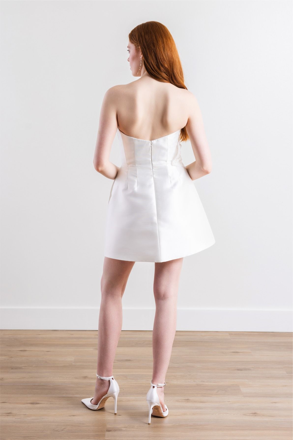 The back of a woman wearing a white dress and heels.