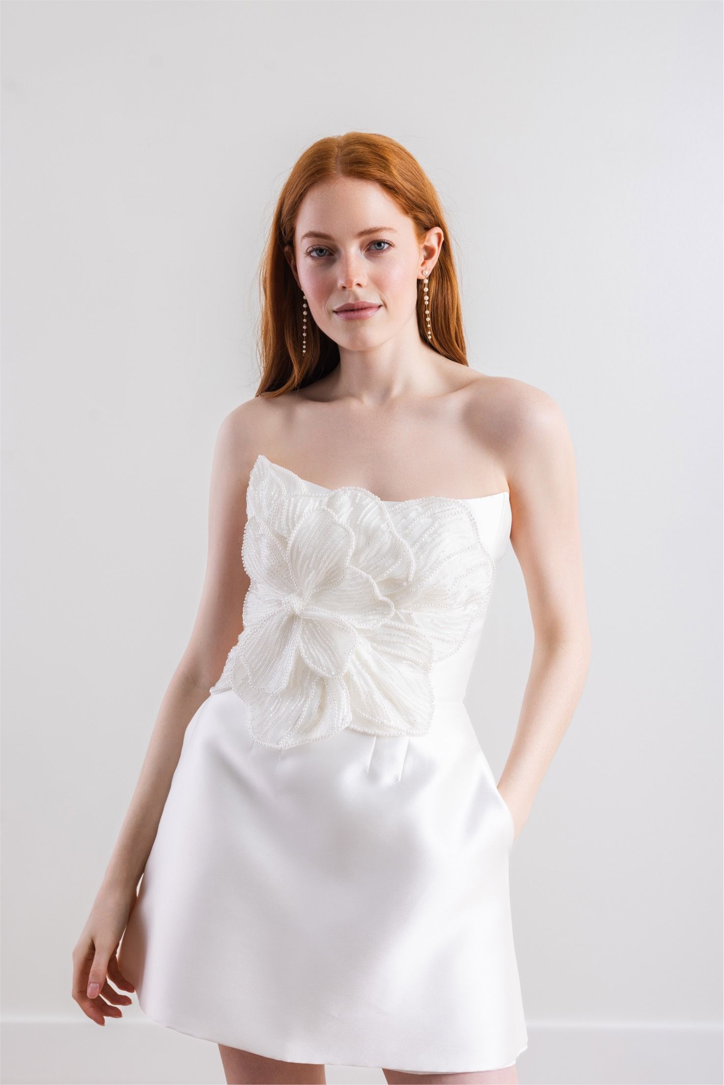 A woman in a white dress is standing in front of a white wall.