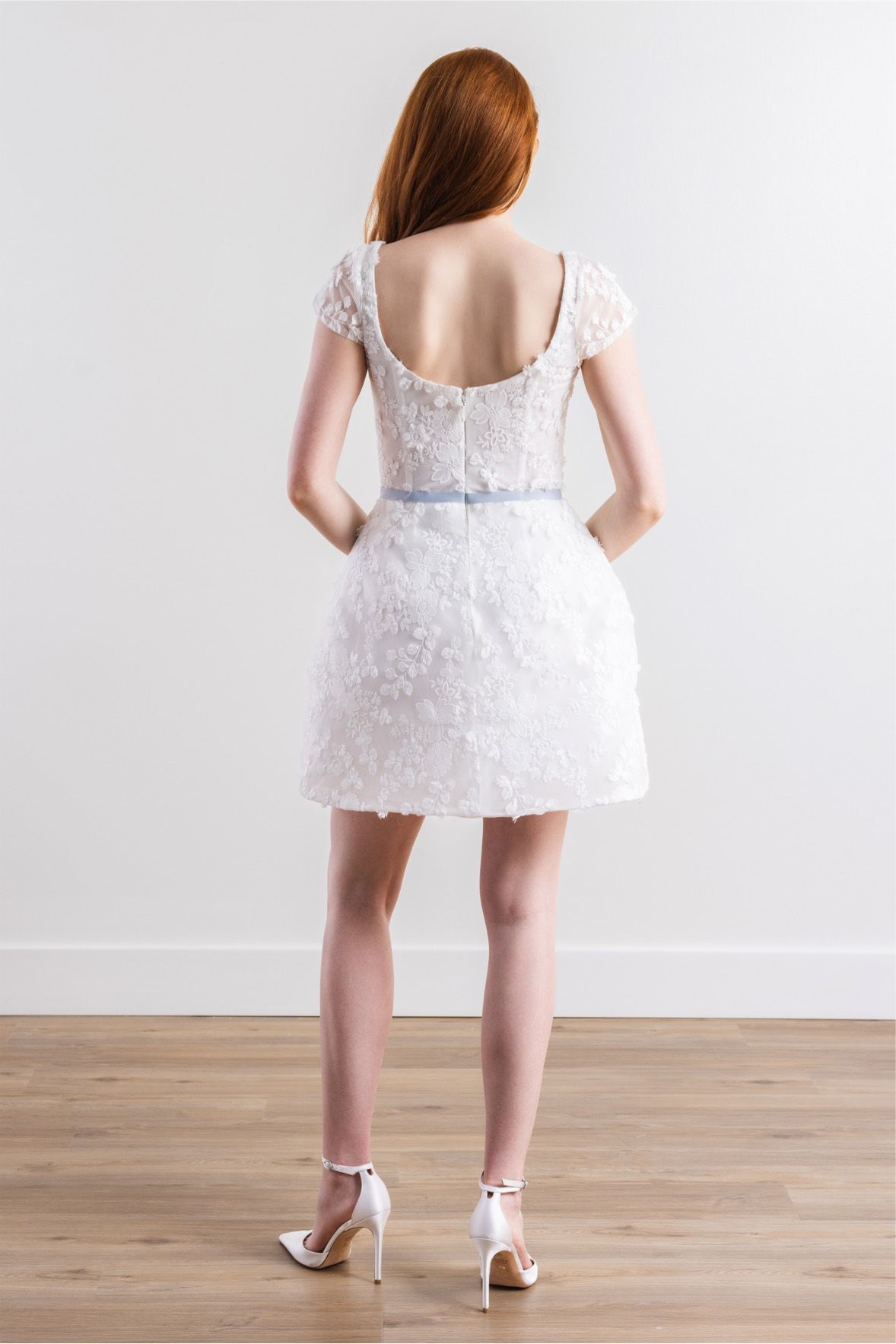 The back of a woman wearing a white lace dress and heels.