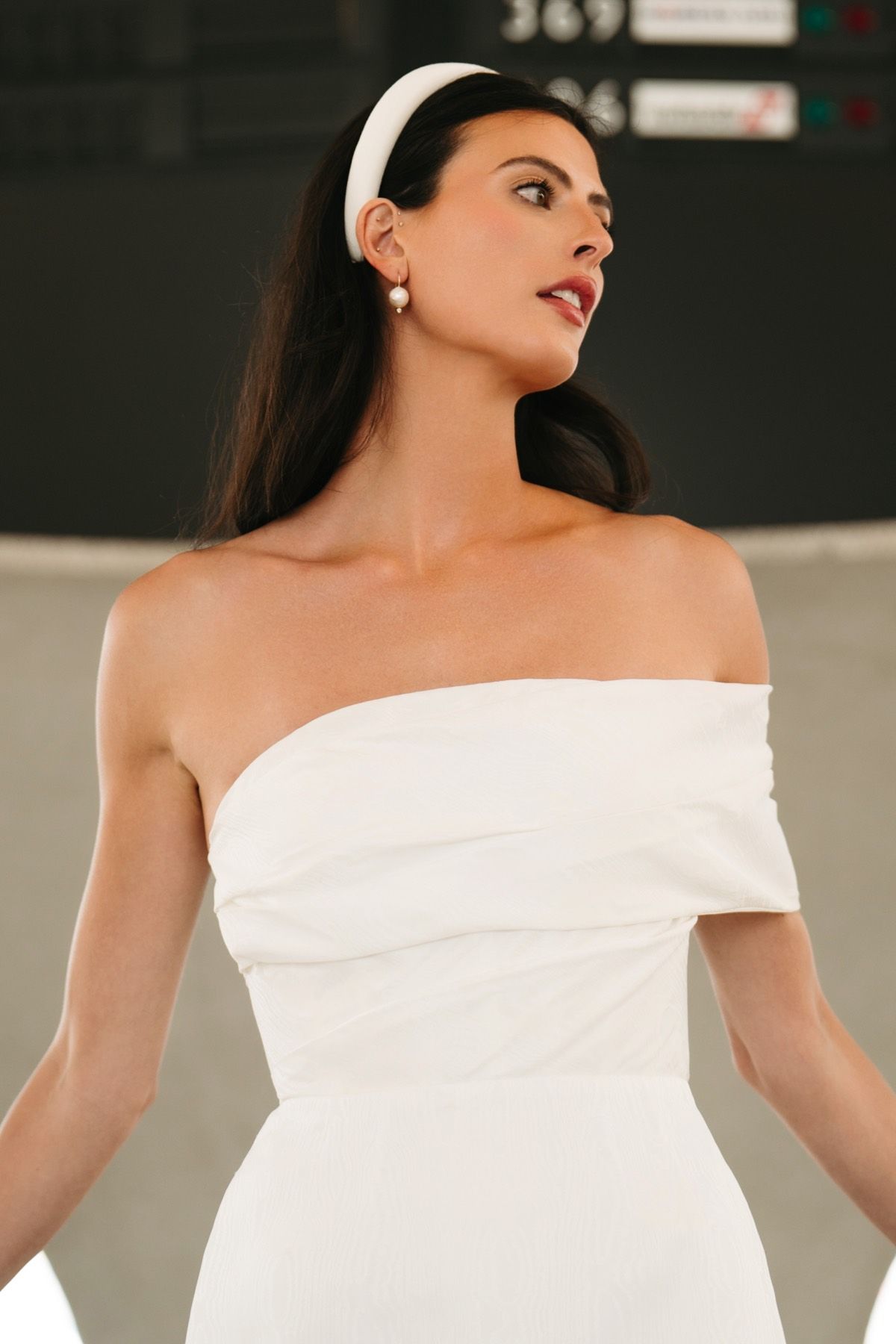 A woman in a white dress and headband is standing in front of a sign.