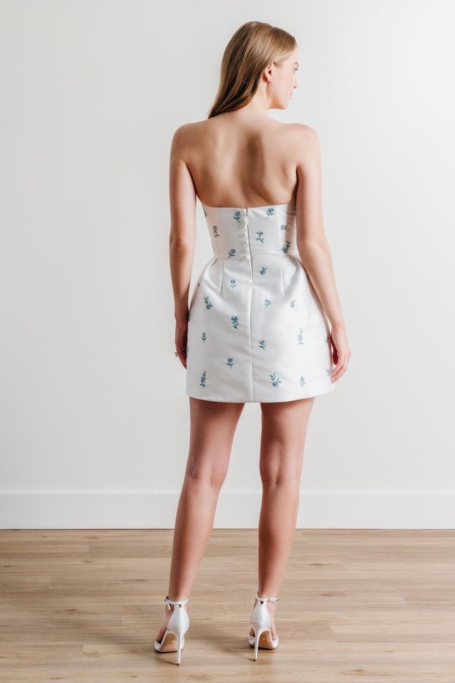 A woman in a white strapless dress is standing on a wooden floor.