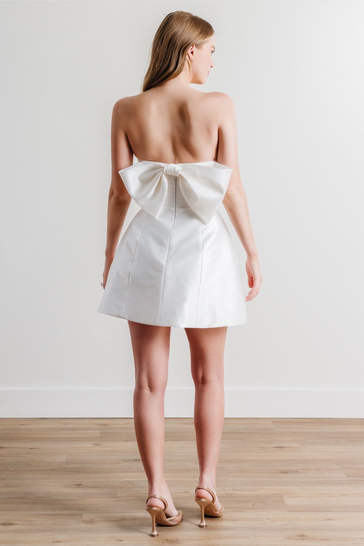 The back of a woman wearing a white dress with a bow on the back.