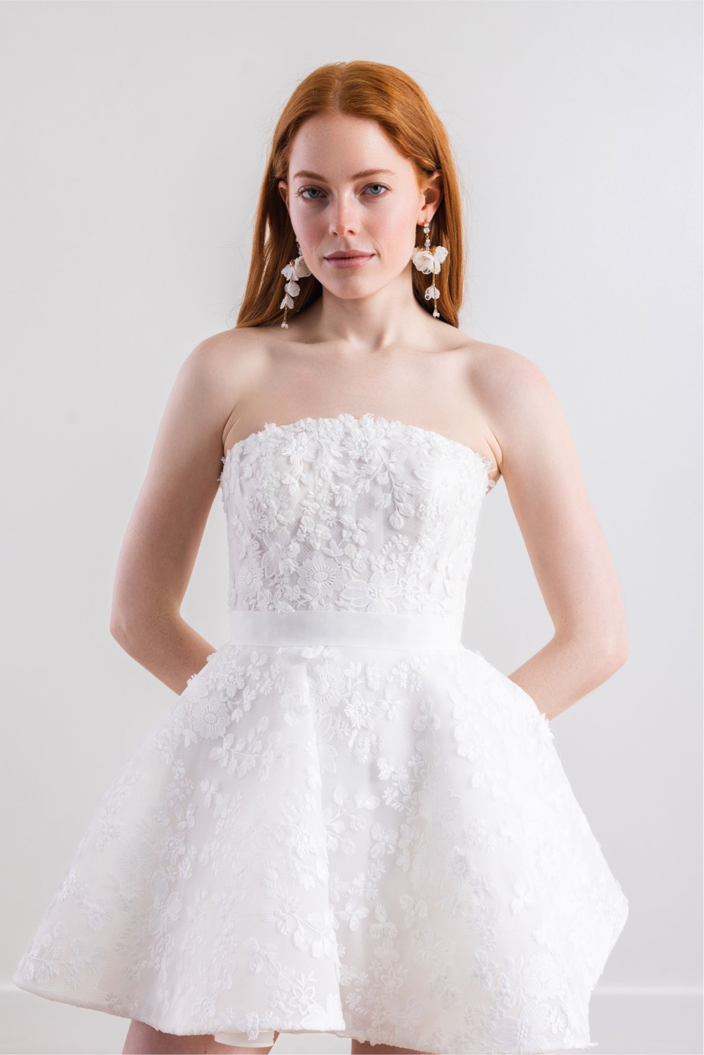 A woman is wearing a white strapless dress and earrings.