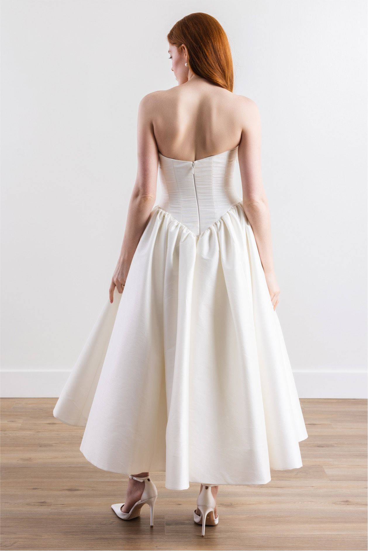 A woman in a white wedding dress is standing on a wooden floor.