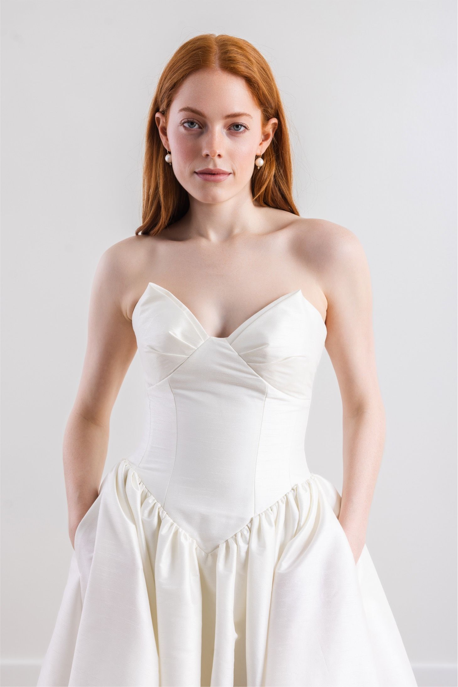 A woman in a white dress is standing with her hands in her pockets.