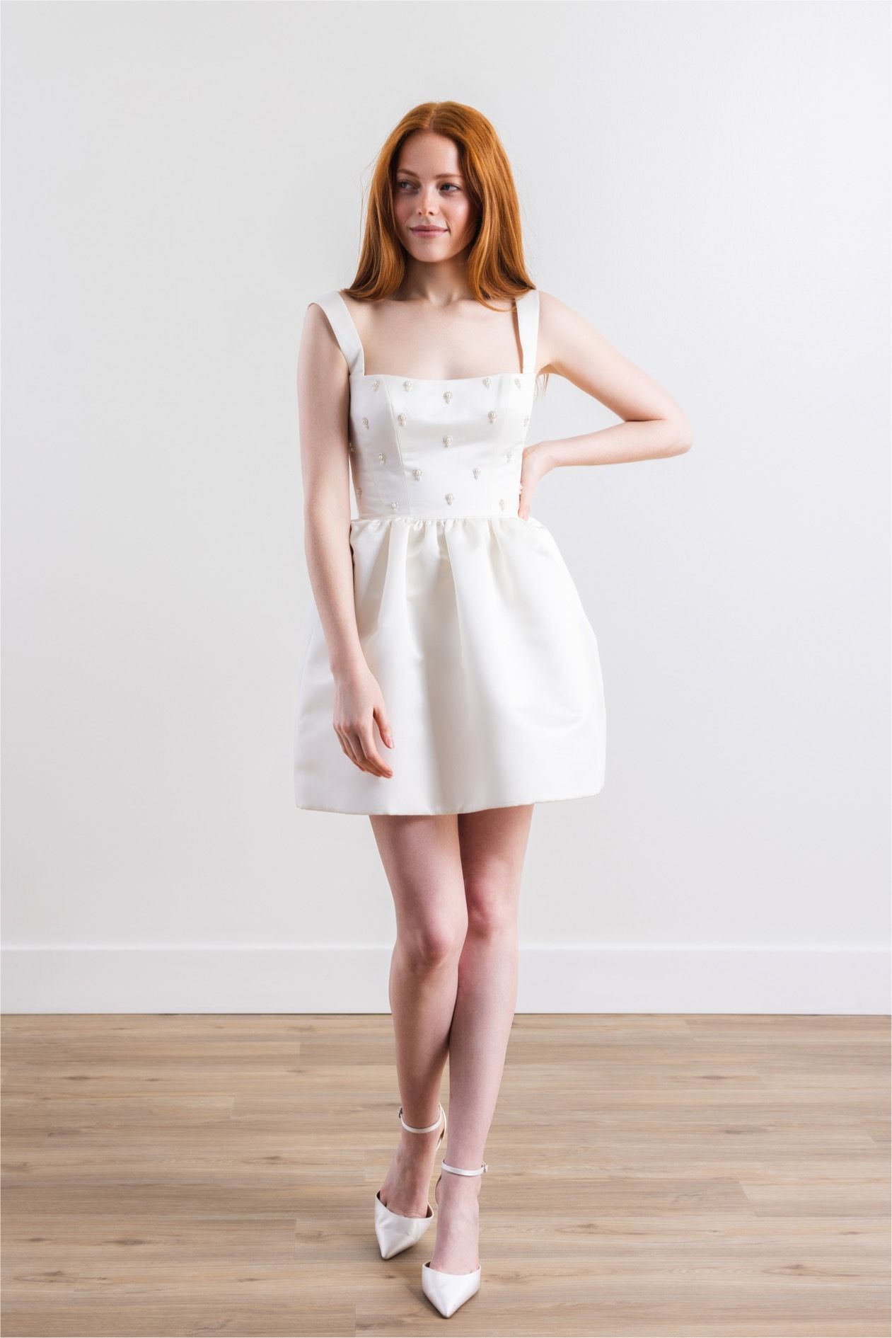 A woman in a white dress is standing on a wooden floor.