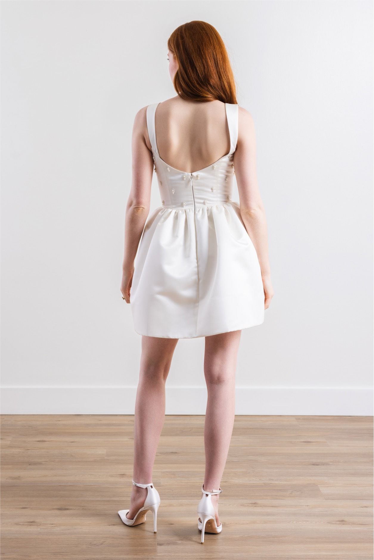 The back of a woman wearing a white dress and heels.