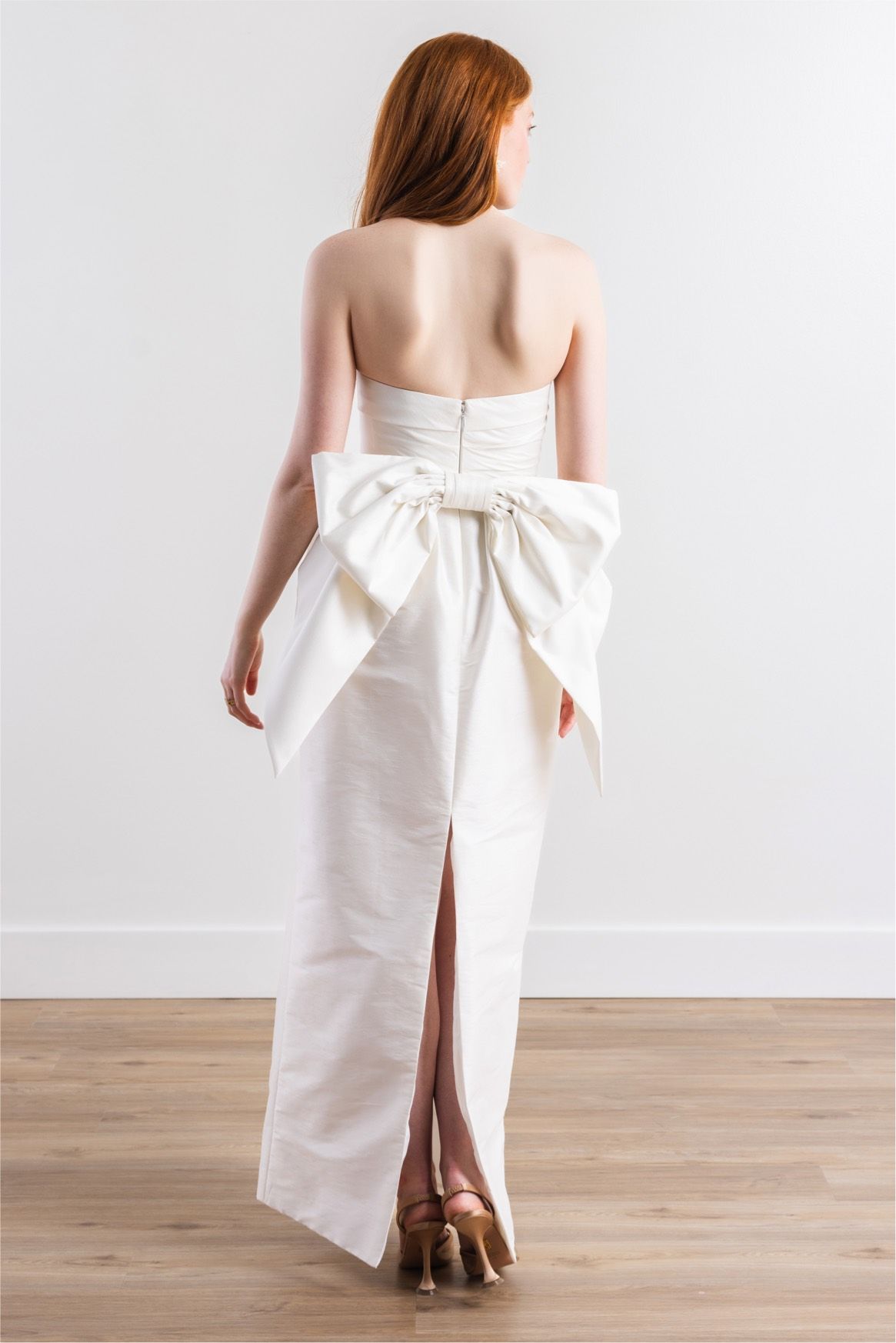 A woman is wearing a white dress with a large bow on the back.