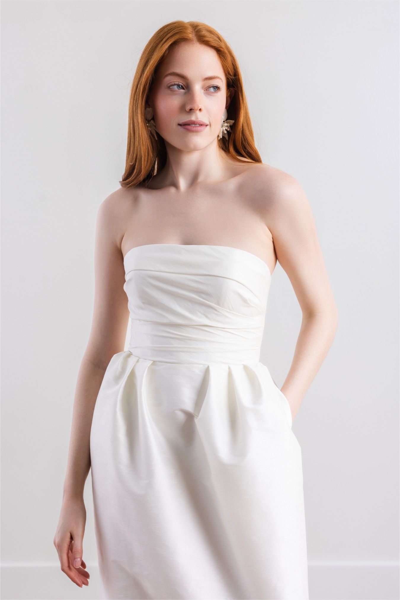 A woman is wearing a white strapless dress with pockets.
