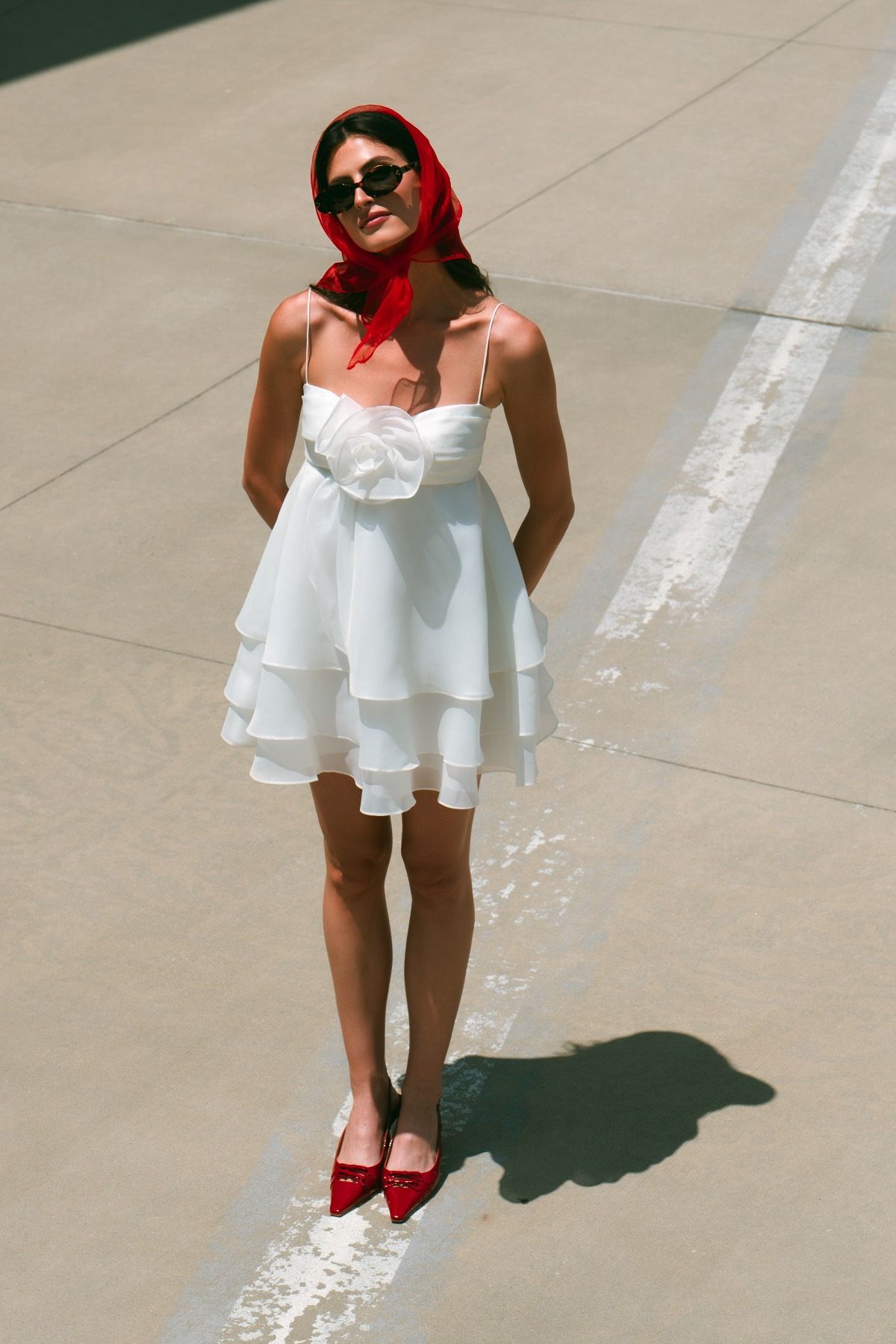 A woman in a white dress and red shoes is standing on a sidewalk.