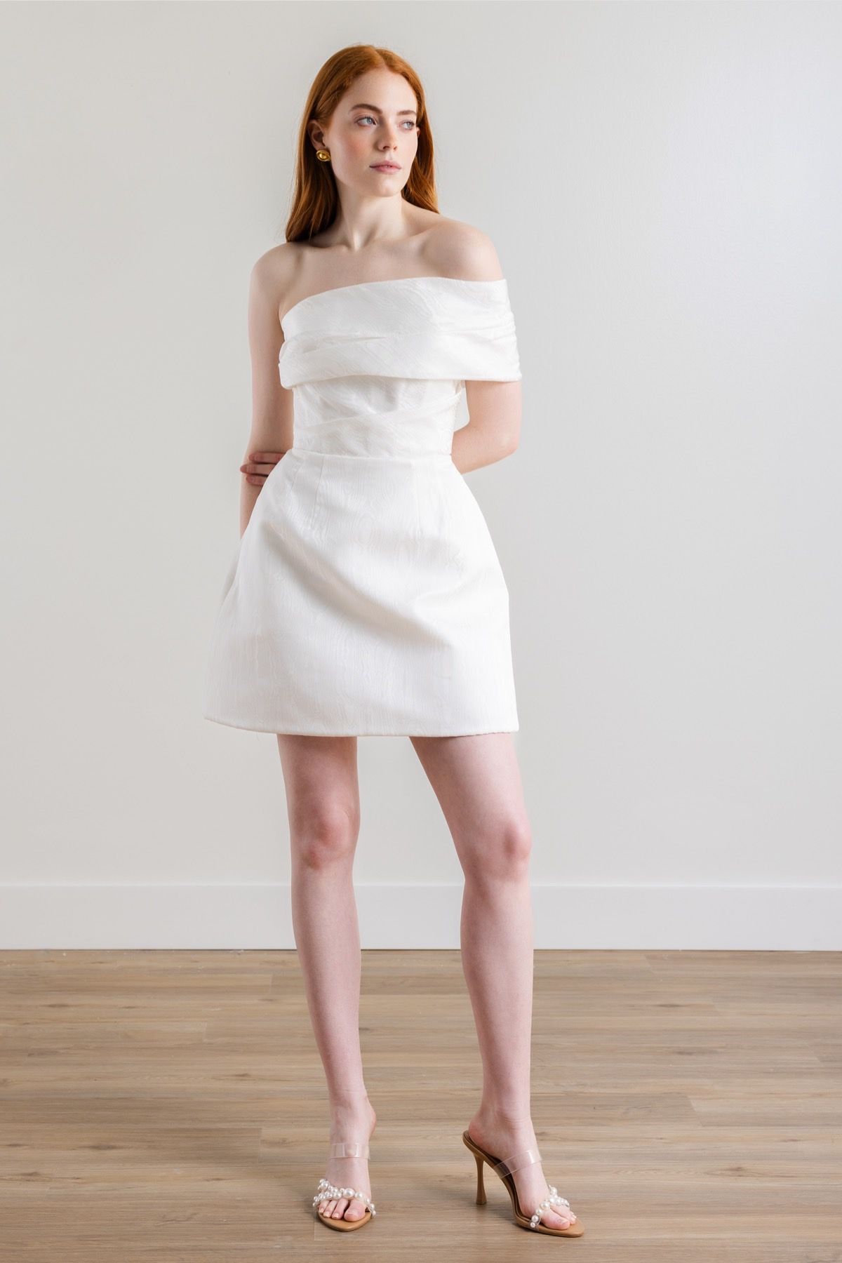 A woman is wearing a white off the shoulder dress and heels.