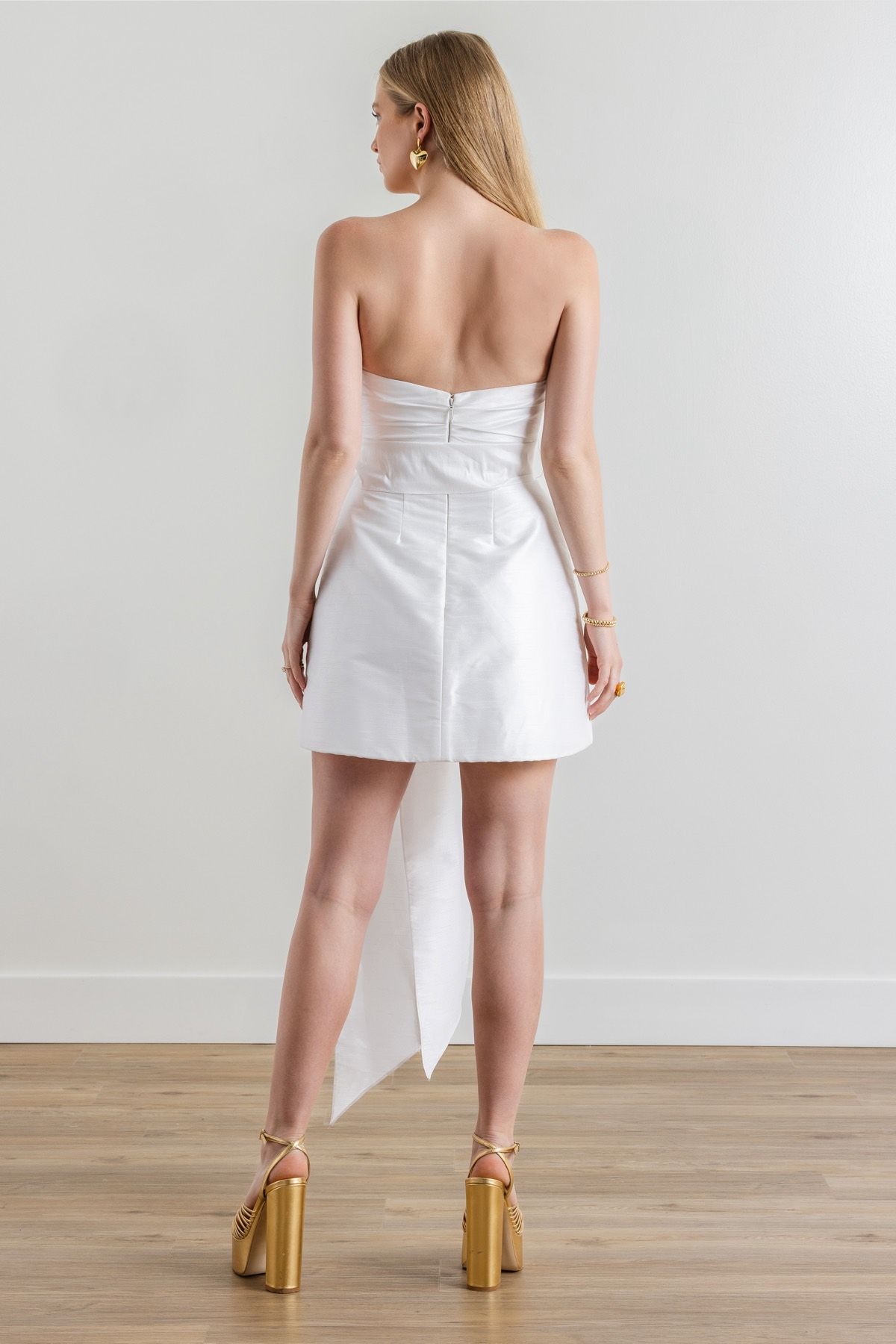 The back of a woman wearing a white strapless dress and heels.