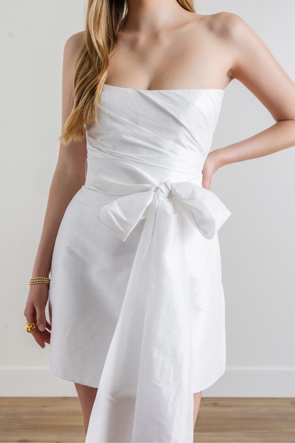 A woman is wearing a white strapless dress with a bow on the waist.