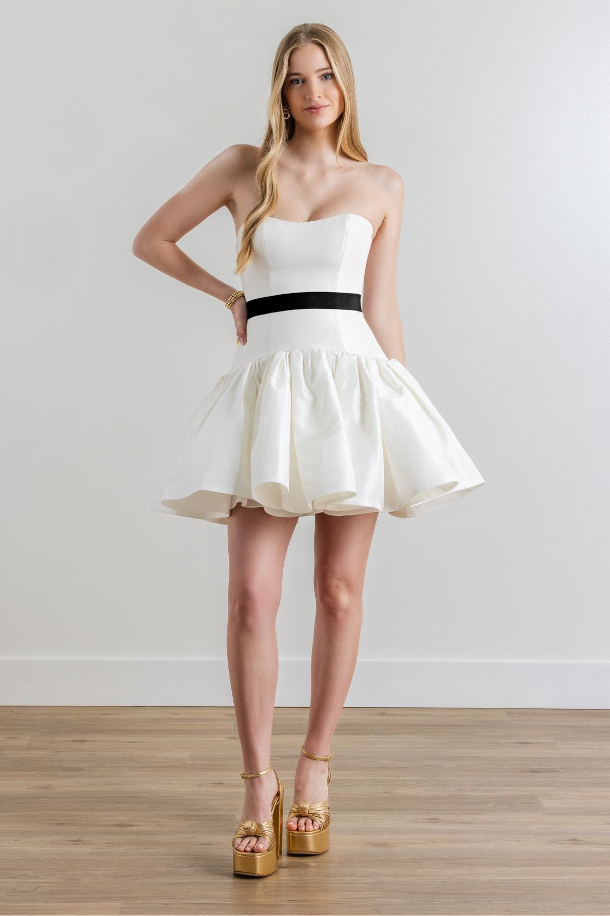 A woman is wearing a white strapless dress with a black belt.