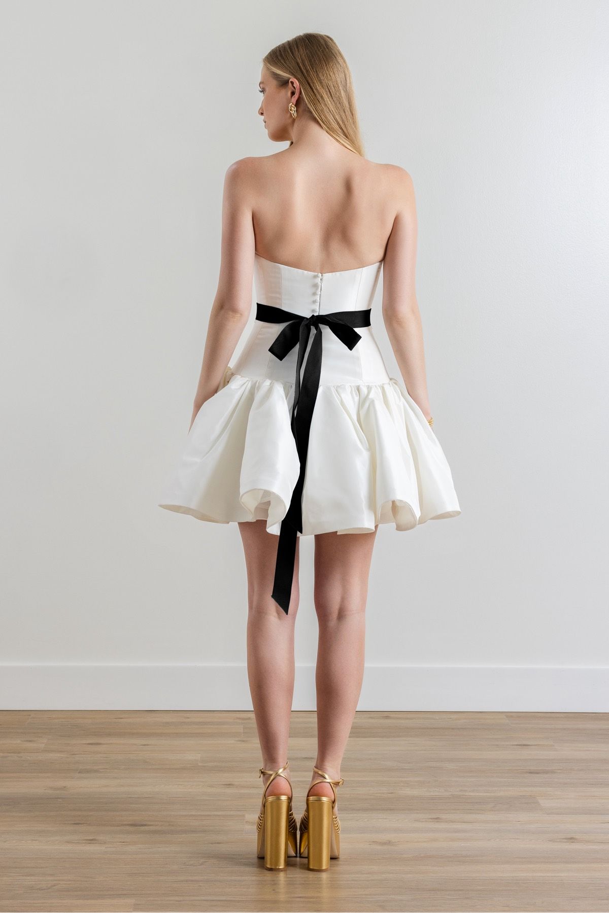 The back of a woman wearing a white dress with a black sash around her waist.
