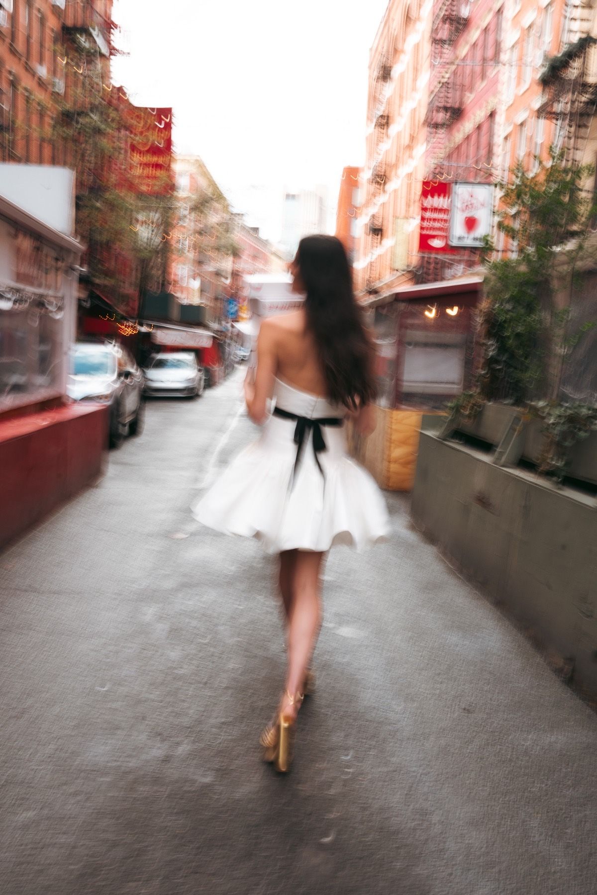 A woman in a white dress is walking down a city street.