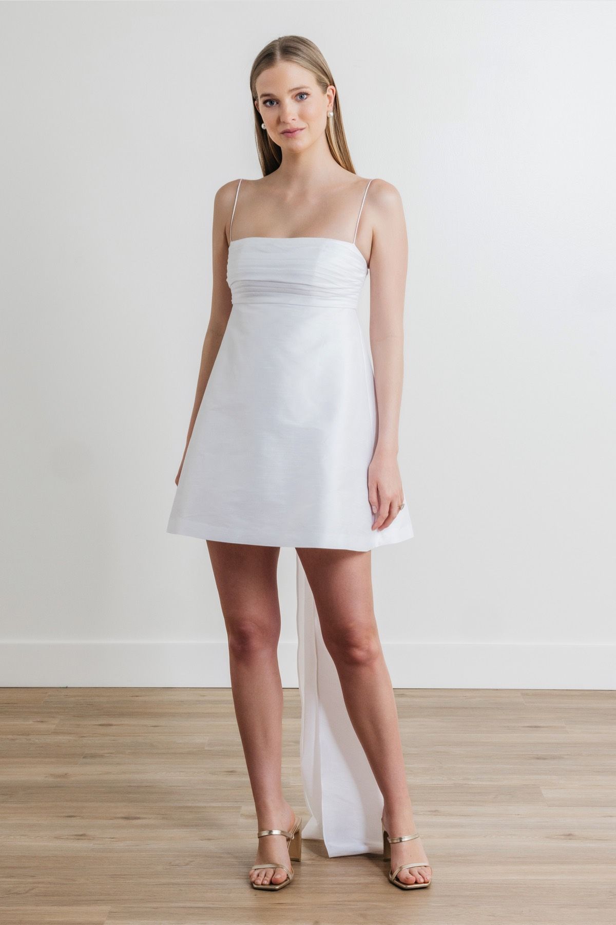 A woman in a white dress is standing on a wooden floor.