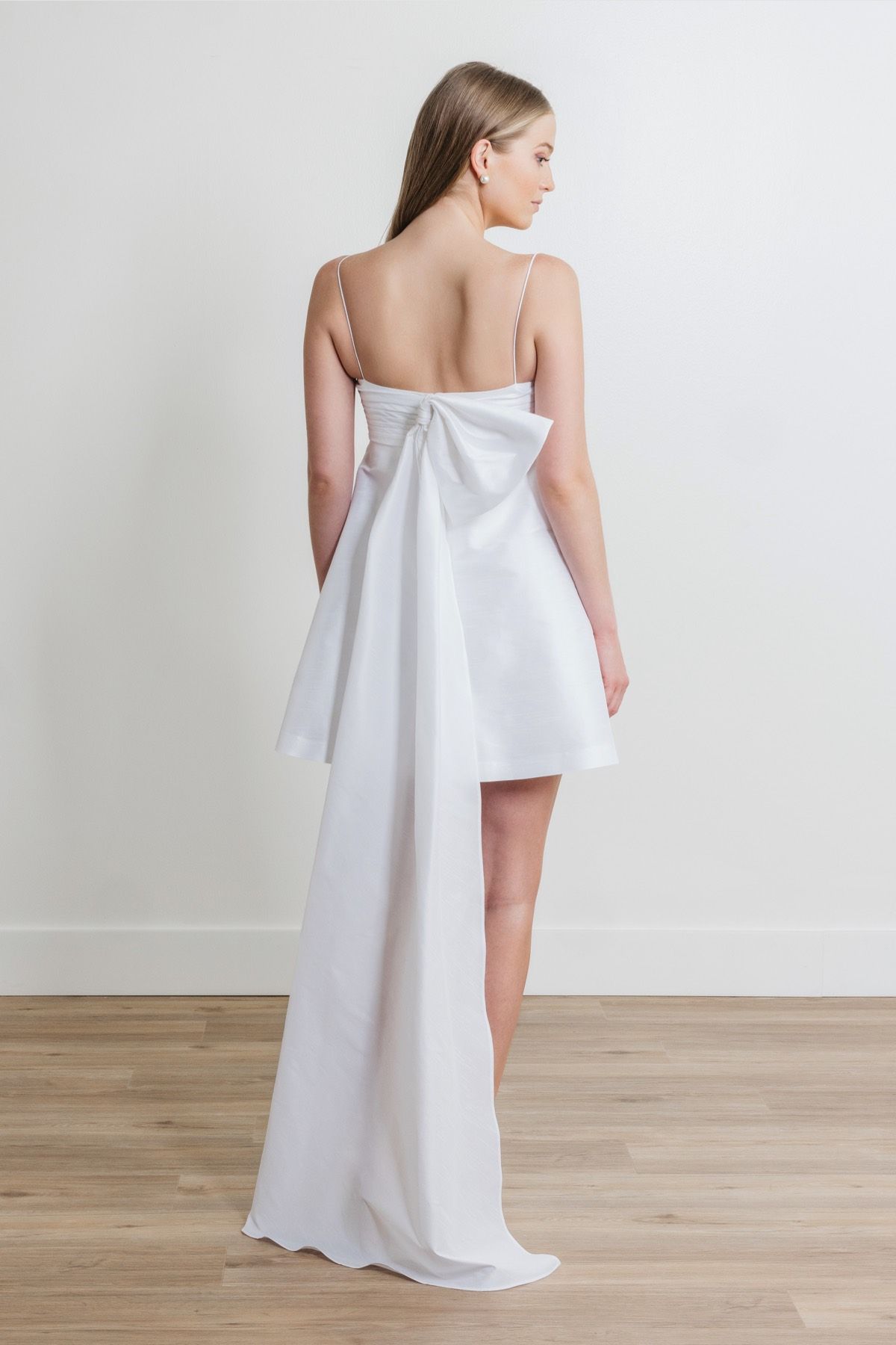 A woman in a white dress with a bow on the back is standing on a wooden floor.