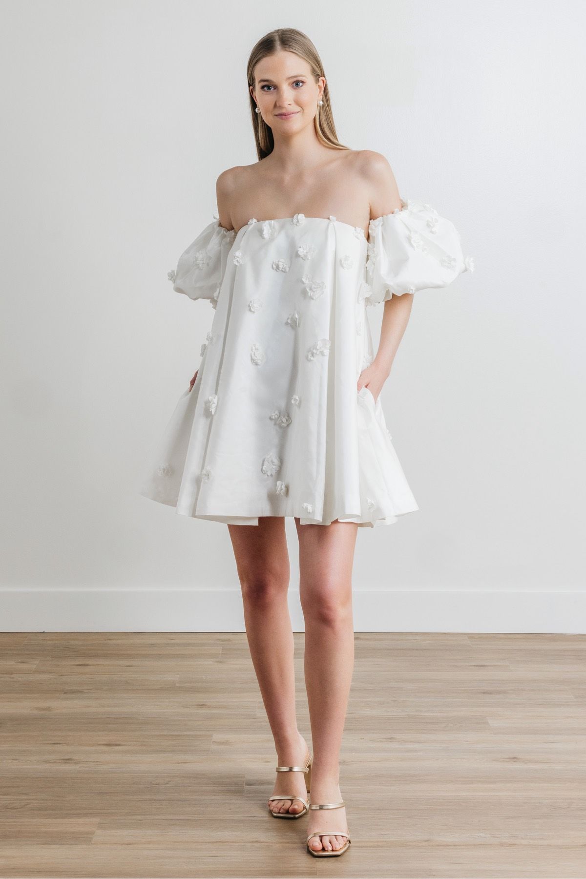 A woman is wearing a white off the shoulder dress with puffed sleeves.