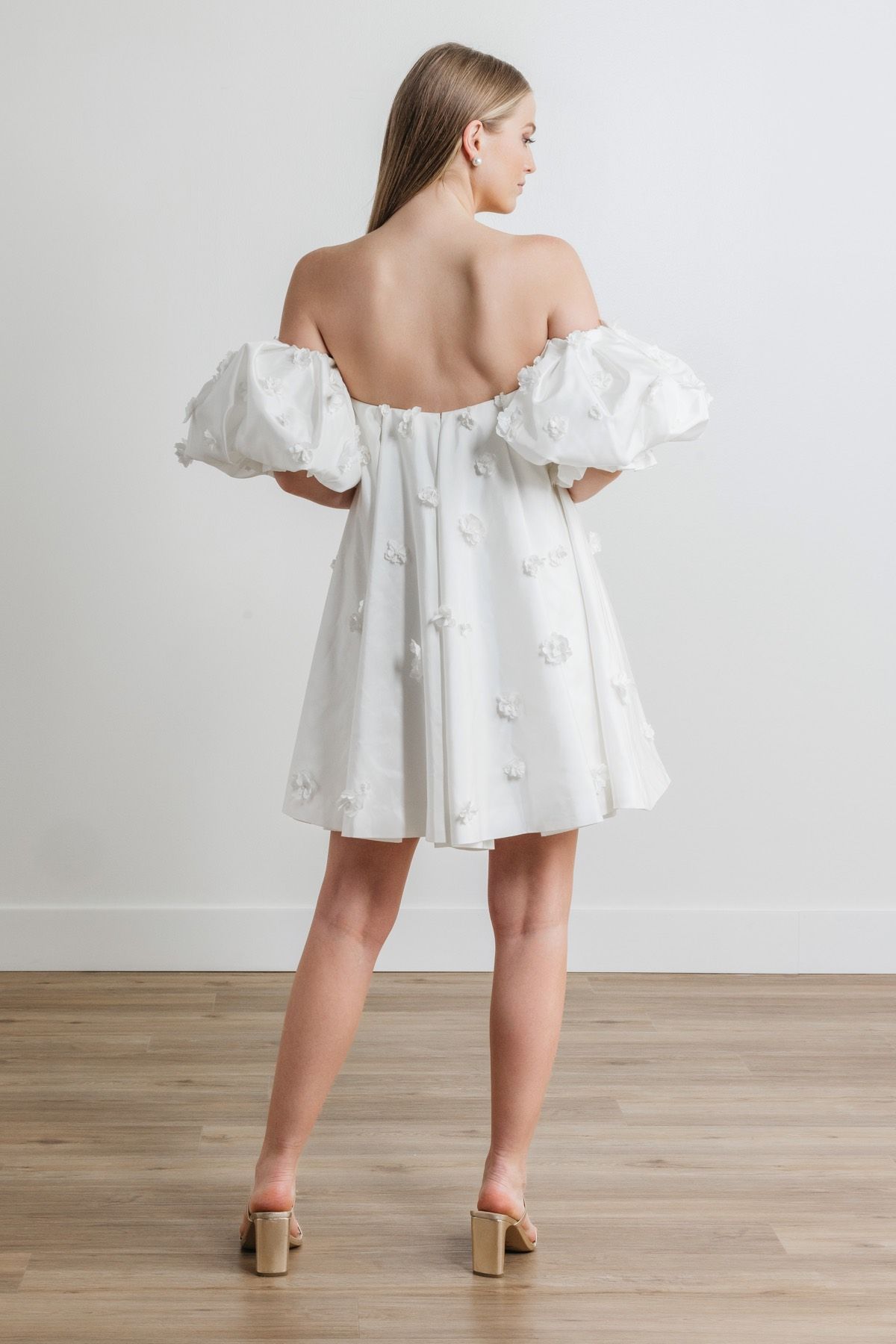The back of a woman wearing a white off the shoulder dress with puffed sleeves.