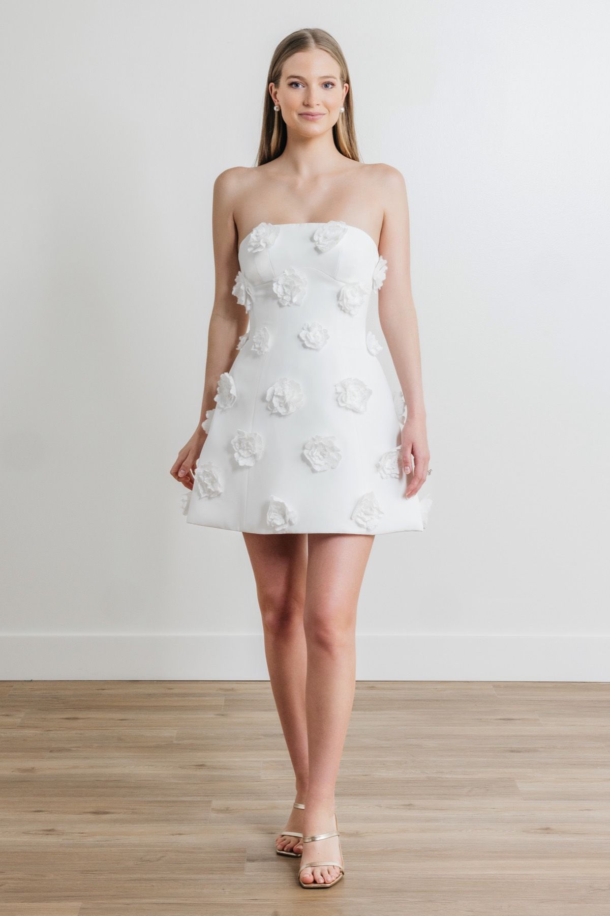 A woman is wearing a white strapless dress with flowers on it.