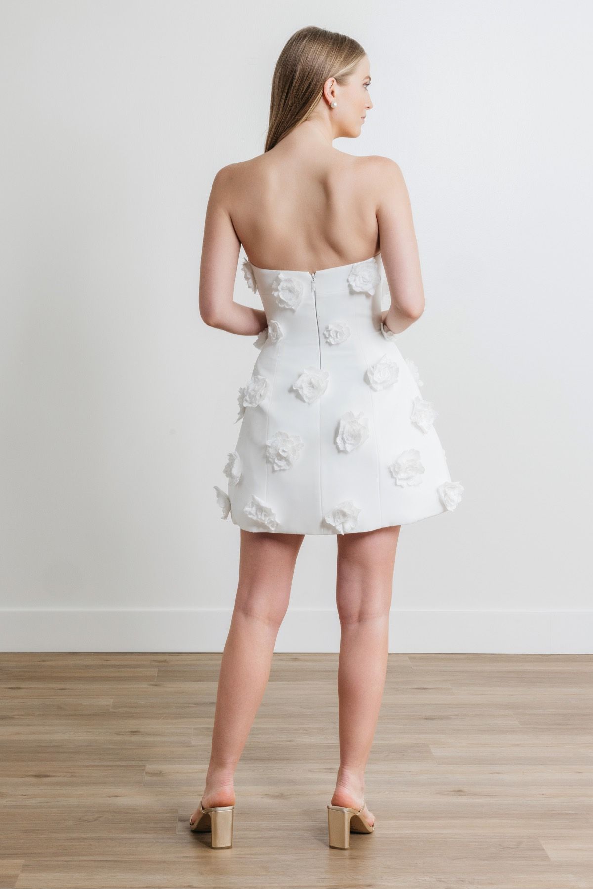 The back of a woman wearing a white strapless dress and heels.