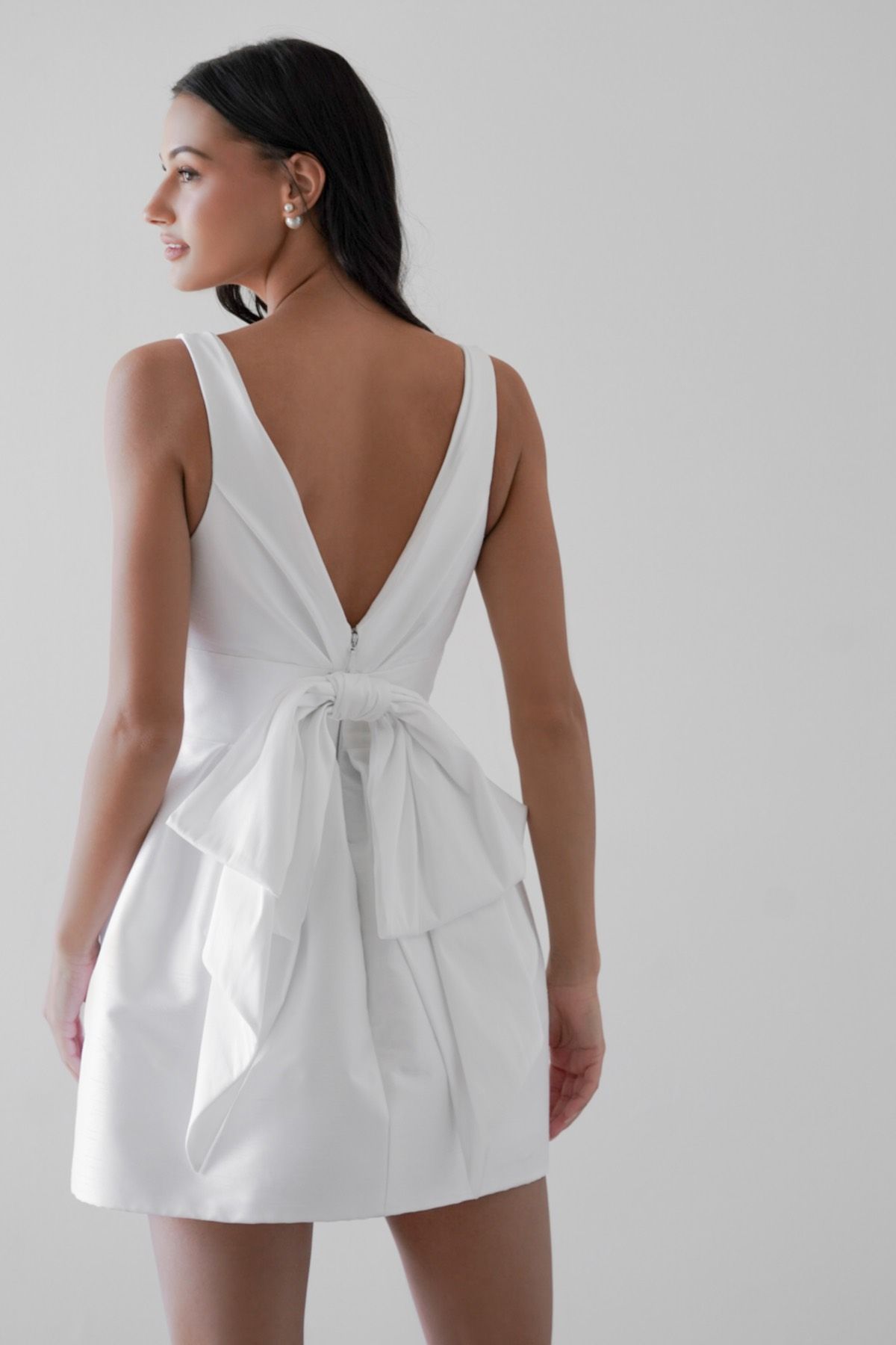 A woman is wearing a white dress with a bow on the back.