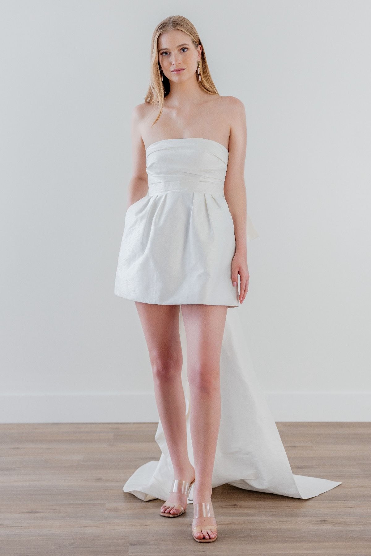 A woman is wearing a short white dress and standing on a wooden floor.
