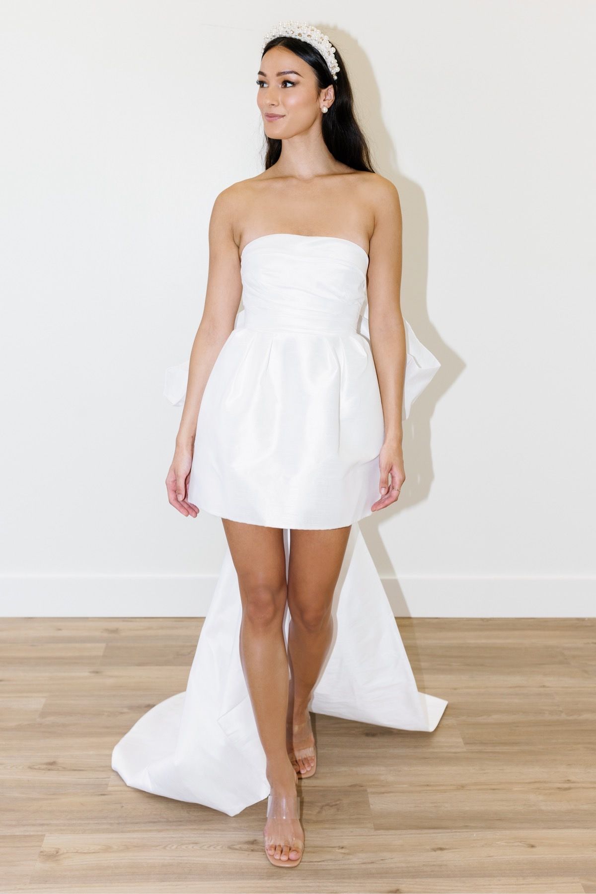 A woman in a white strapless dress is standing on a wooden floor.