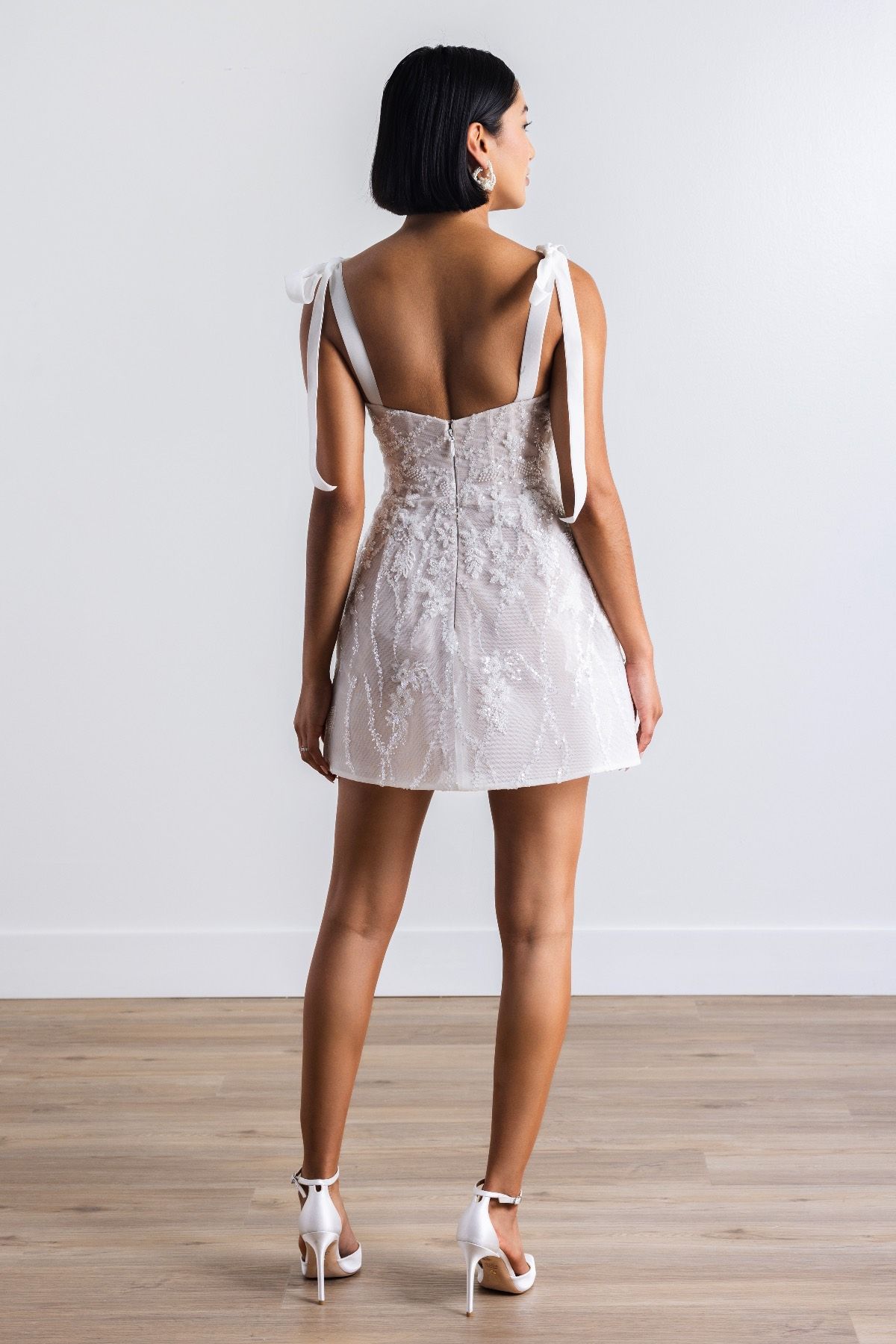 The back of a woman wearing a white dress and heels.