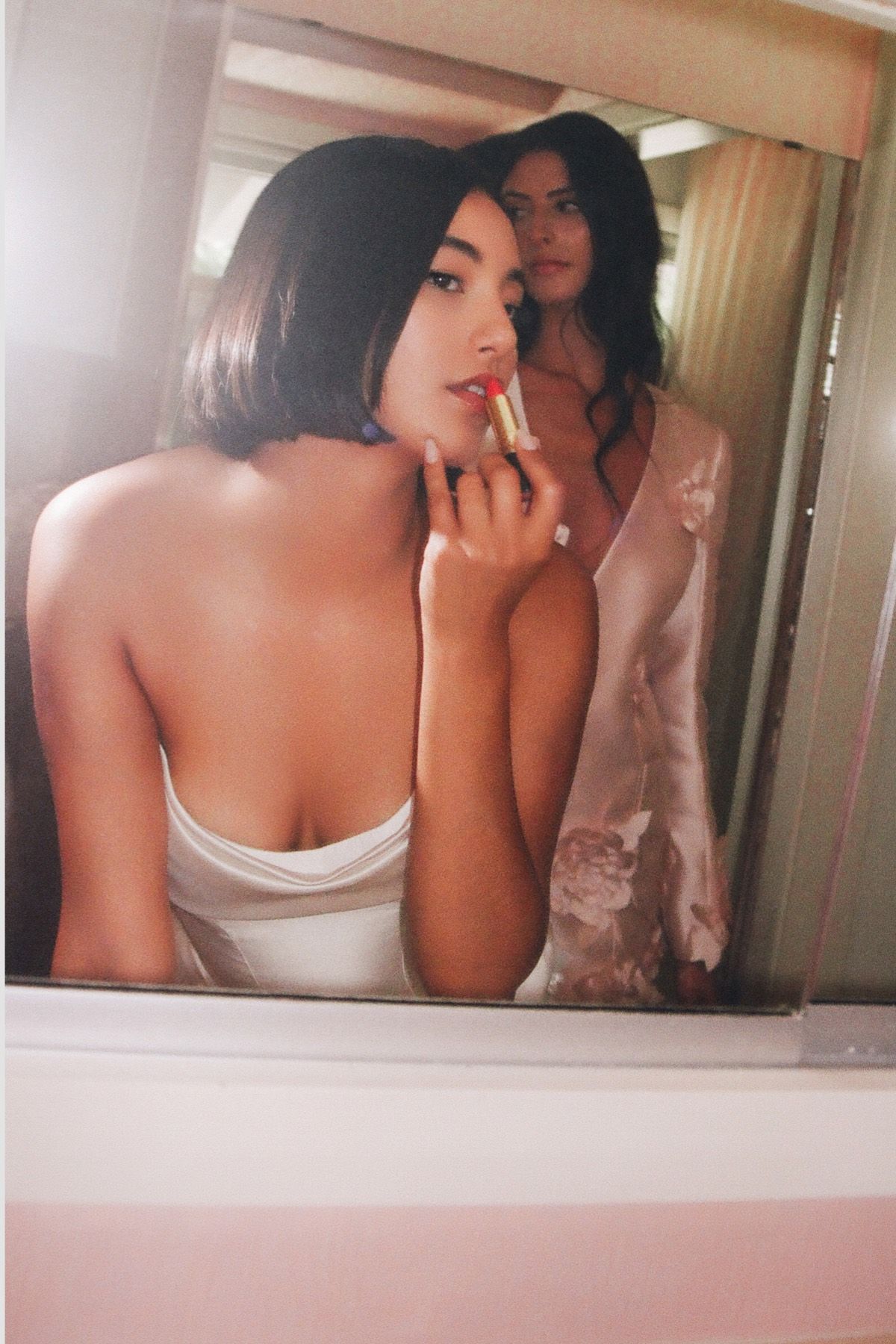 A woman is applying lipstick in front of a mirror.