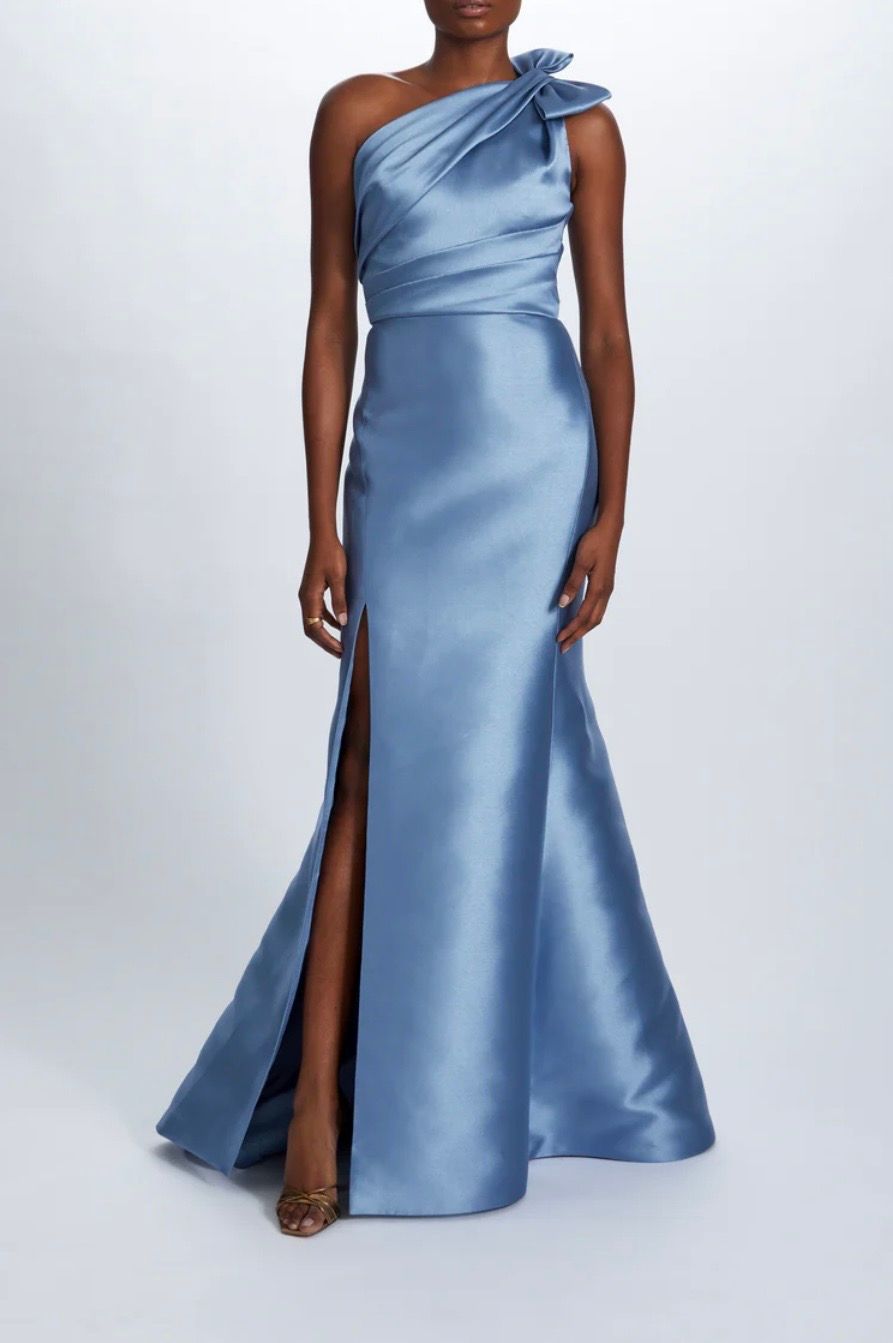 A woman is wearing a light blue one shoulder dress with a high slit.