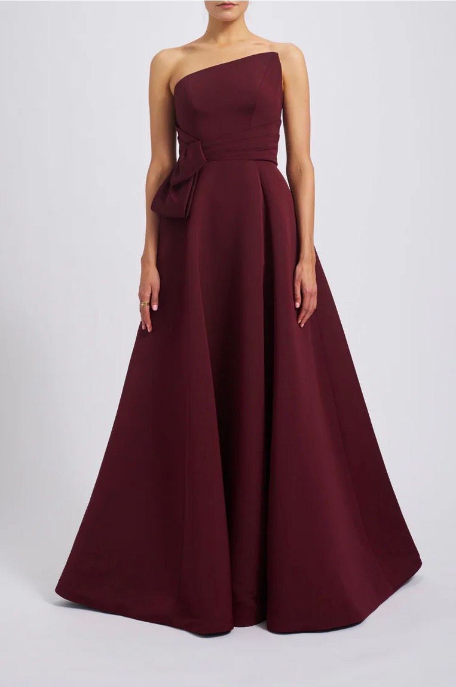 A woman is wearing a burgundy one shoulder dress.