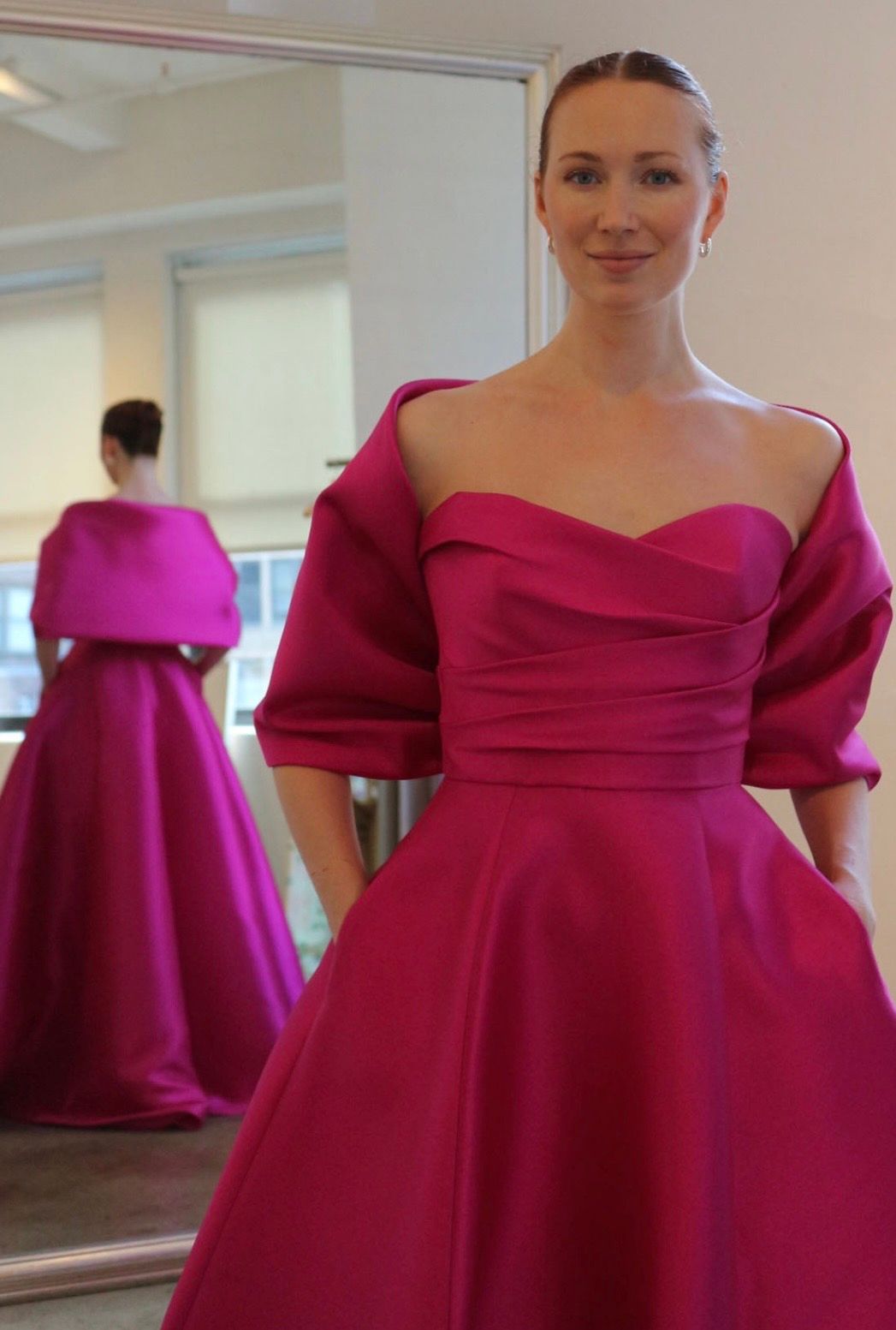 A woman in a pink dress is standing in front of a mirror.
