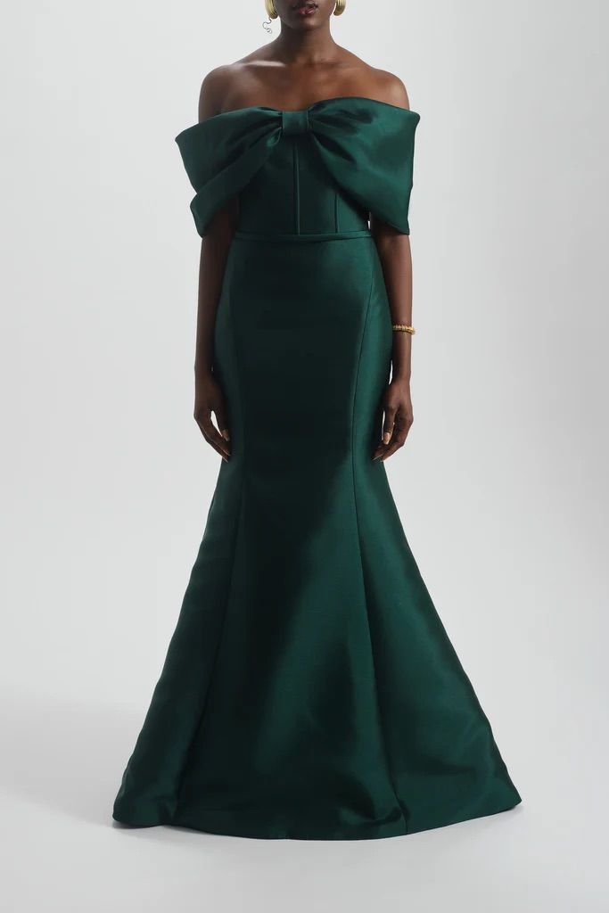A woman is wearing a green off the shoulder dress with a bow