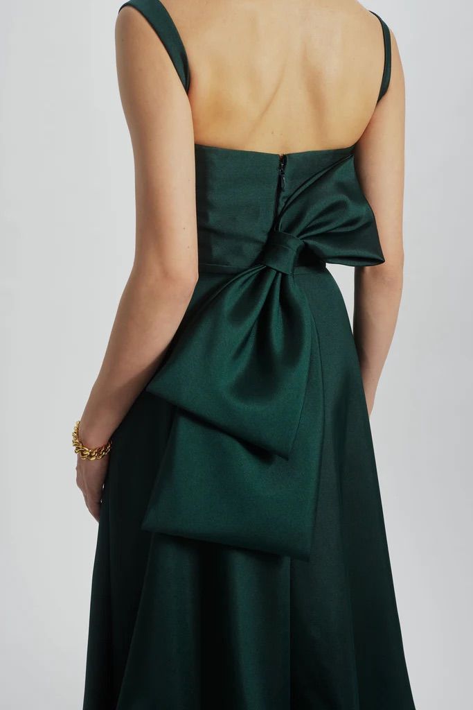 A woman is wearing a green dress with a bow on the back.