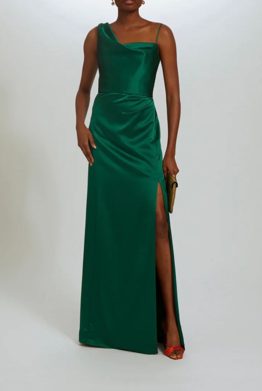 A woman is wearing a green satin one shoulder dress with a high slit.