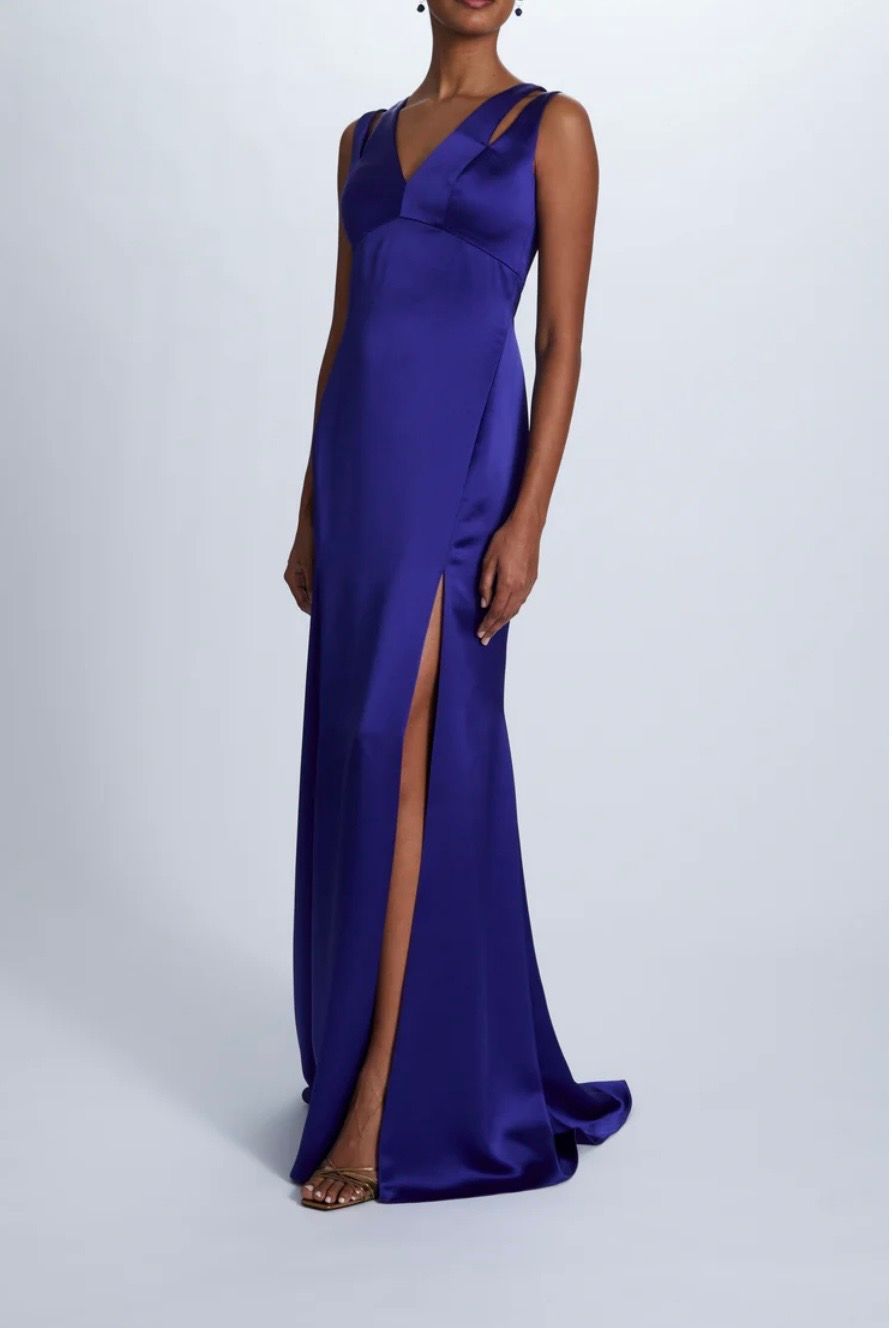 A woman is wearing a blue satin dress with a high slit.