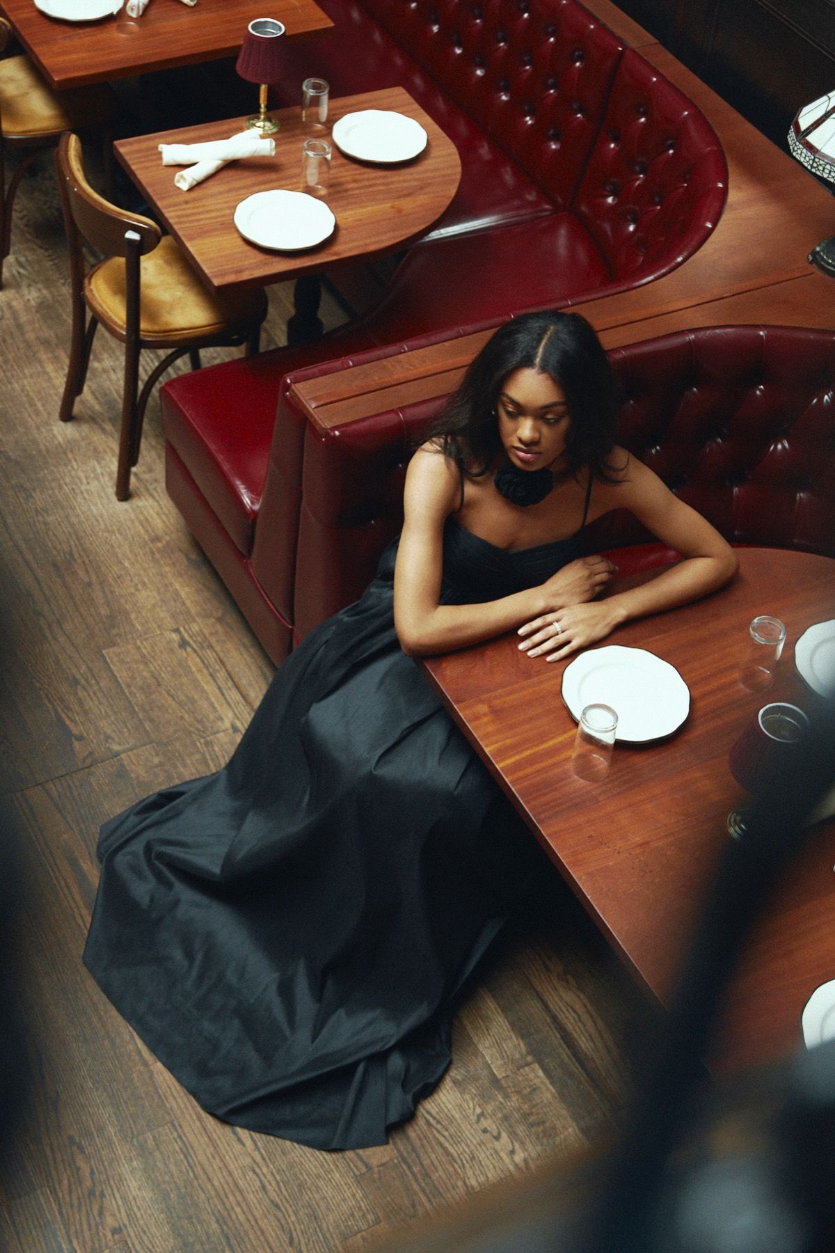 A woman in a black dress is sitting at a table in a restaurant.
