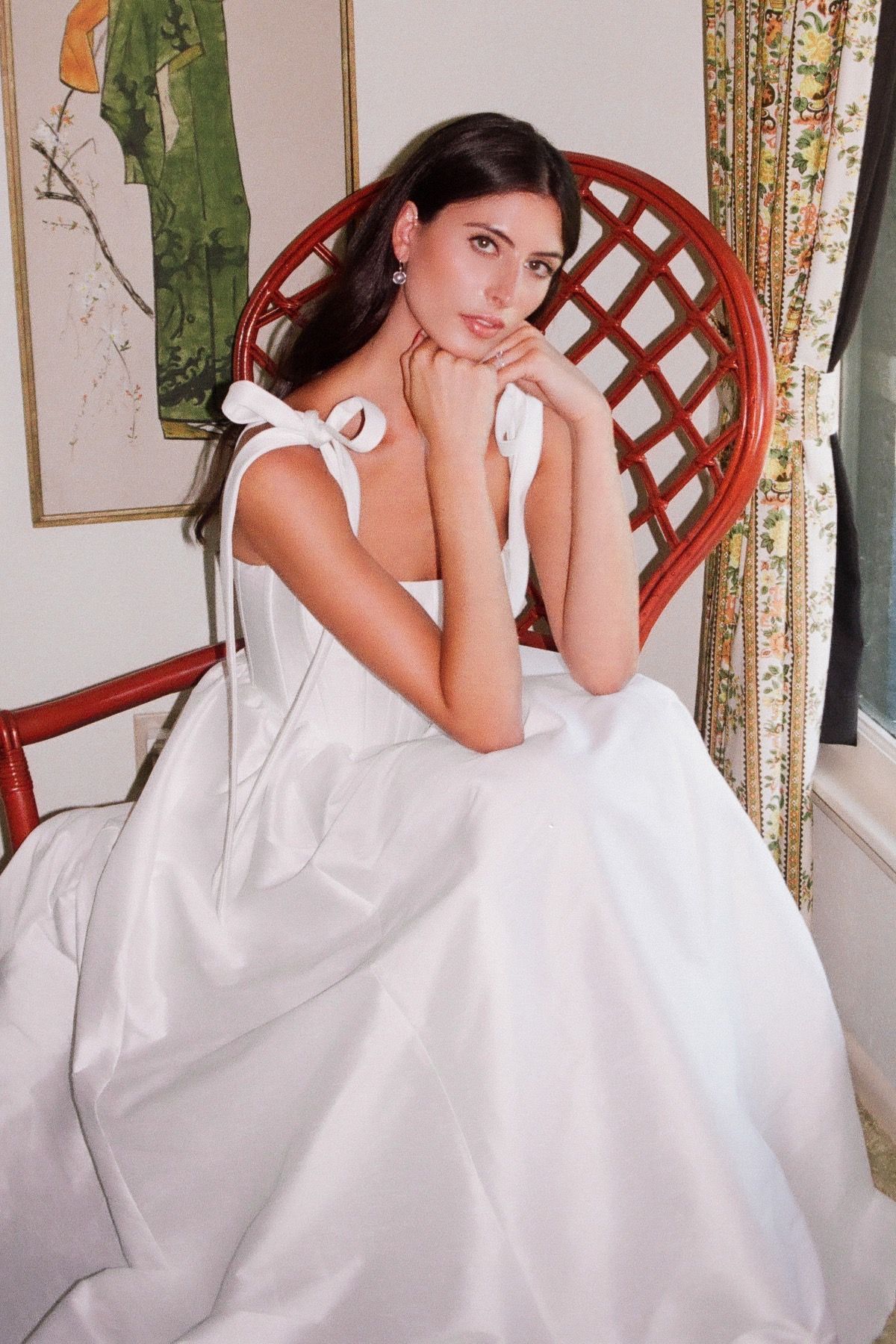 A woman in a white dress is sitting in a red chair.