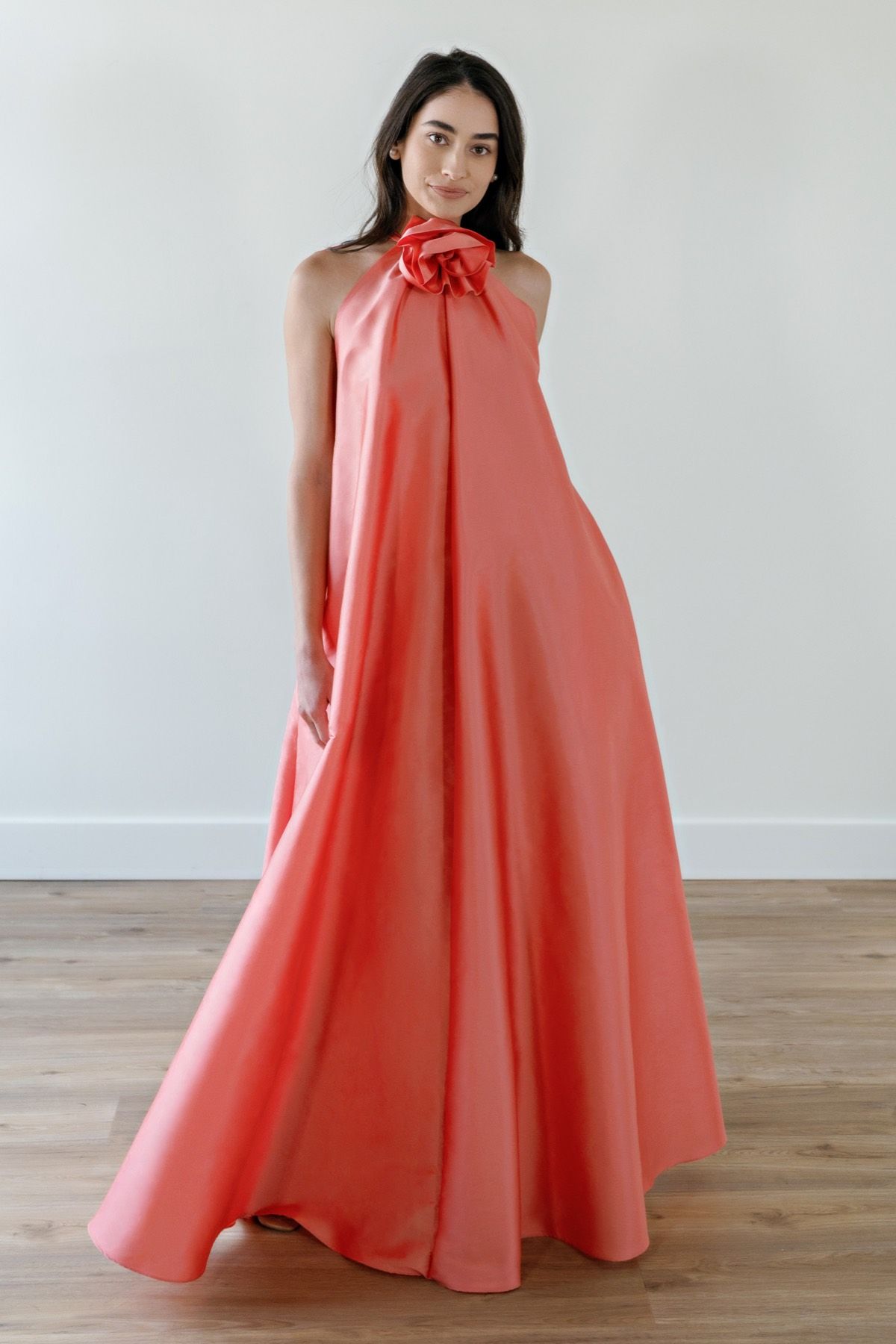 A woman in a long coral dress is standing on a wooden floor.