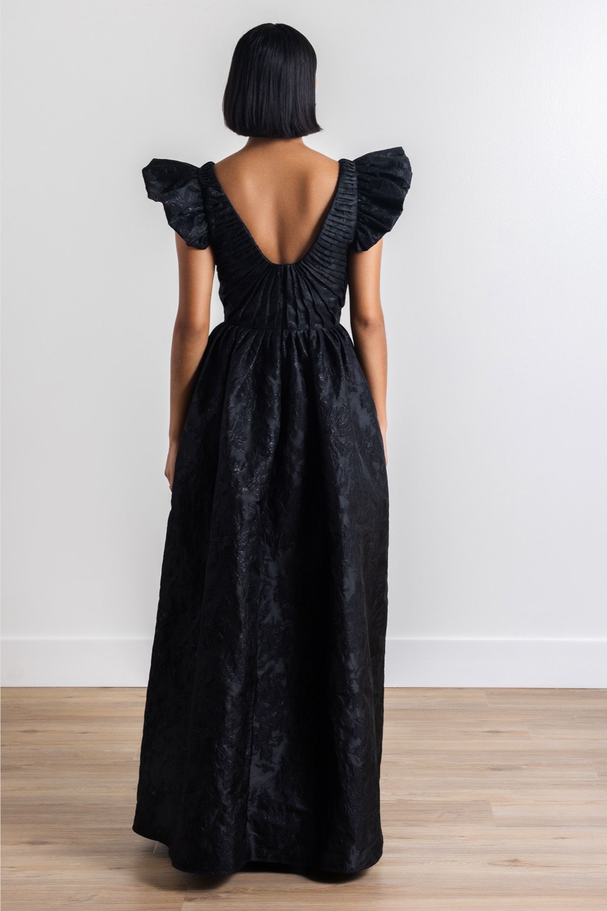 The back of a woman wearing a black dress with ruffled sleeves.