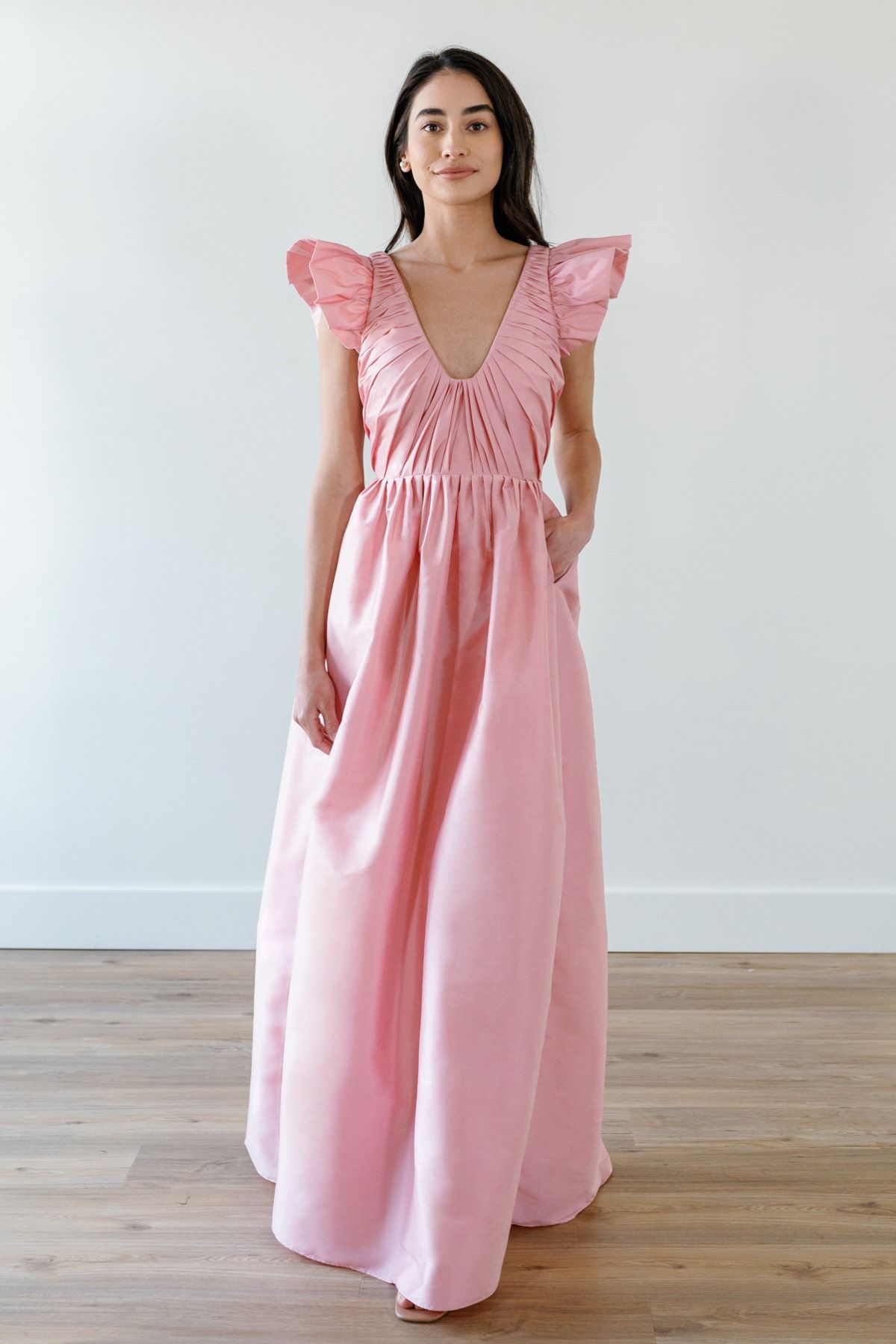 A woman in a pink dress is standing on a wooden floor.